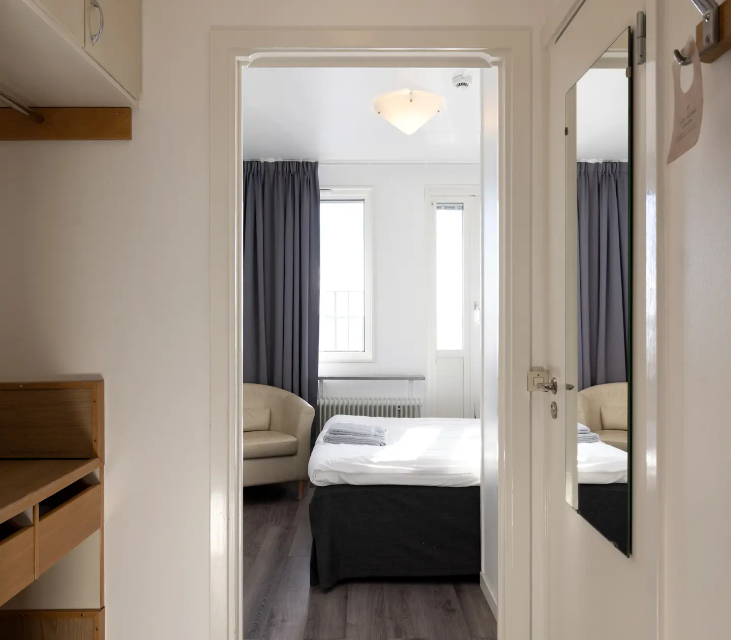 Hotellrum med säng, beige läderfåtölj och spegel