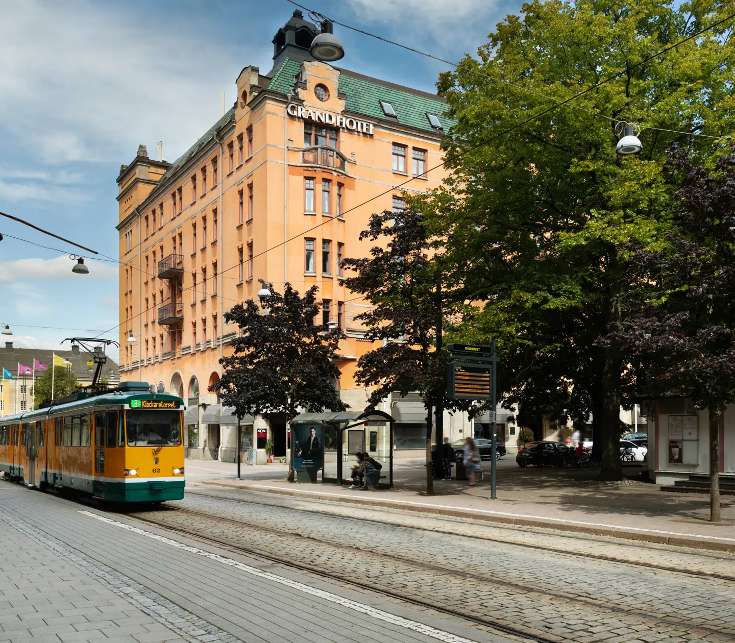 Orange fasaden av Elite Grand Hotel i Norrköping med träd och spårvagn framför
