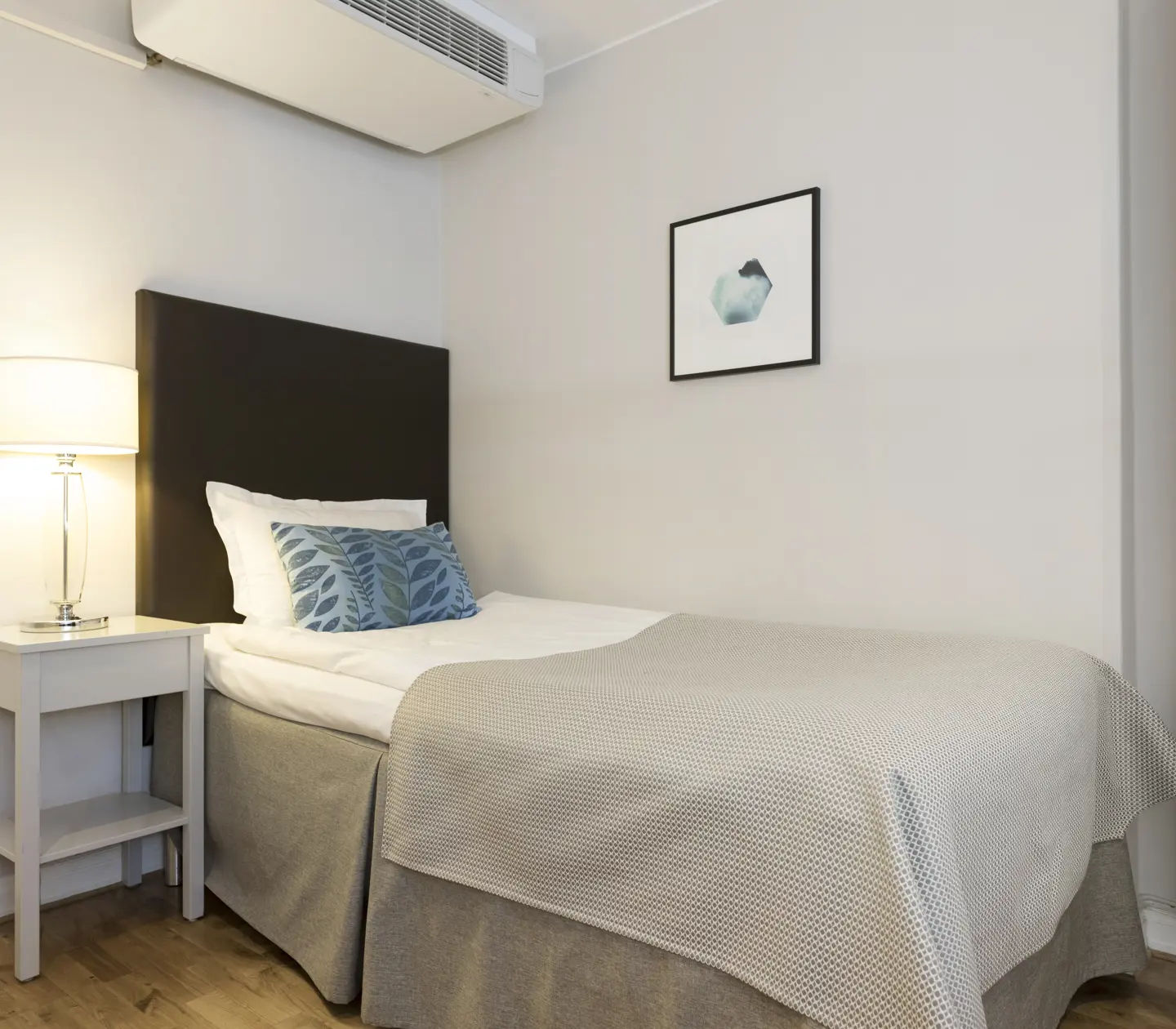 Ljust hotellrum med säng, nattduksbord och sänglampa