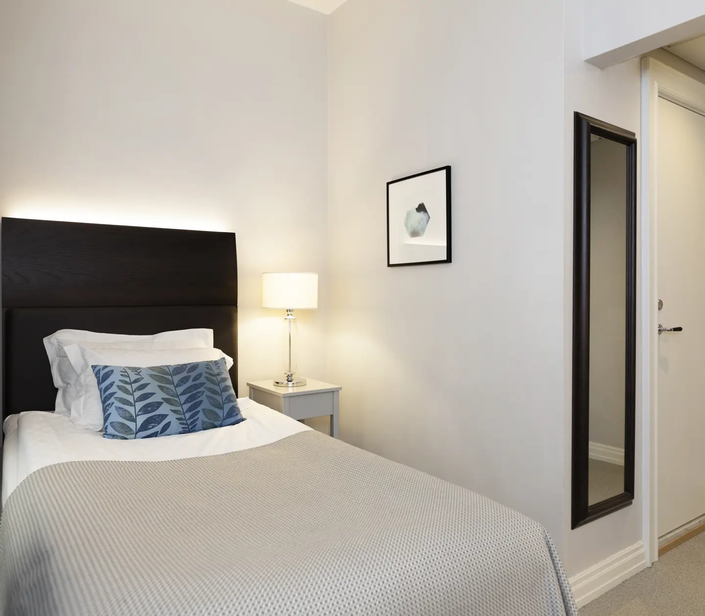 Ljust hotellrum med säng, sänglampa och spegel