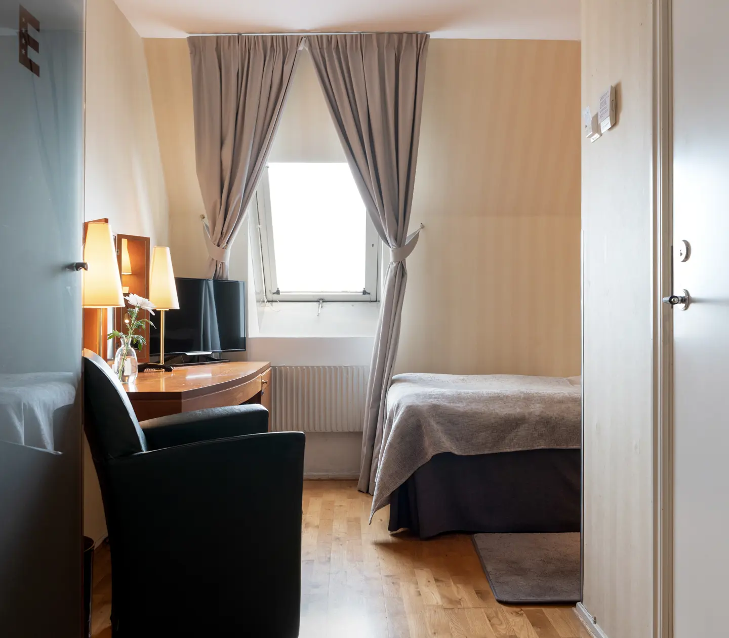 Ljust hotellrum med säng, snedfönster och skrivbord