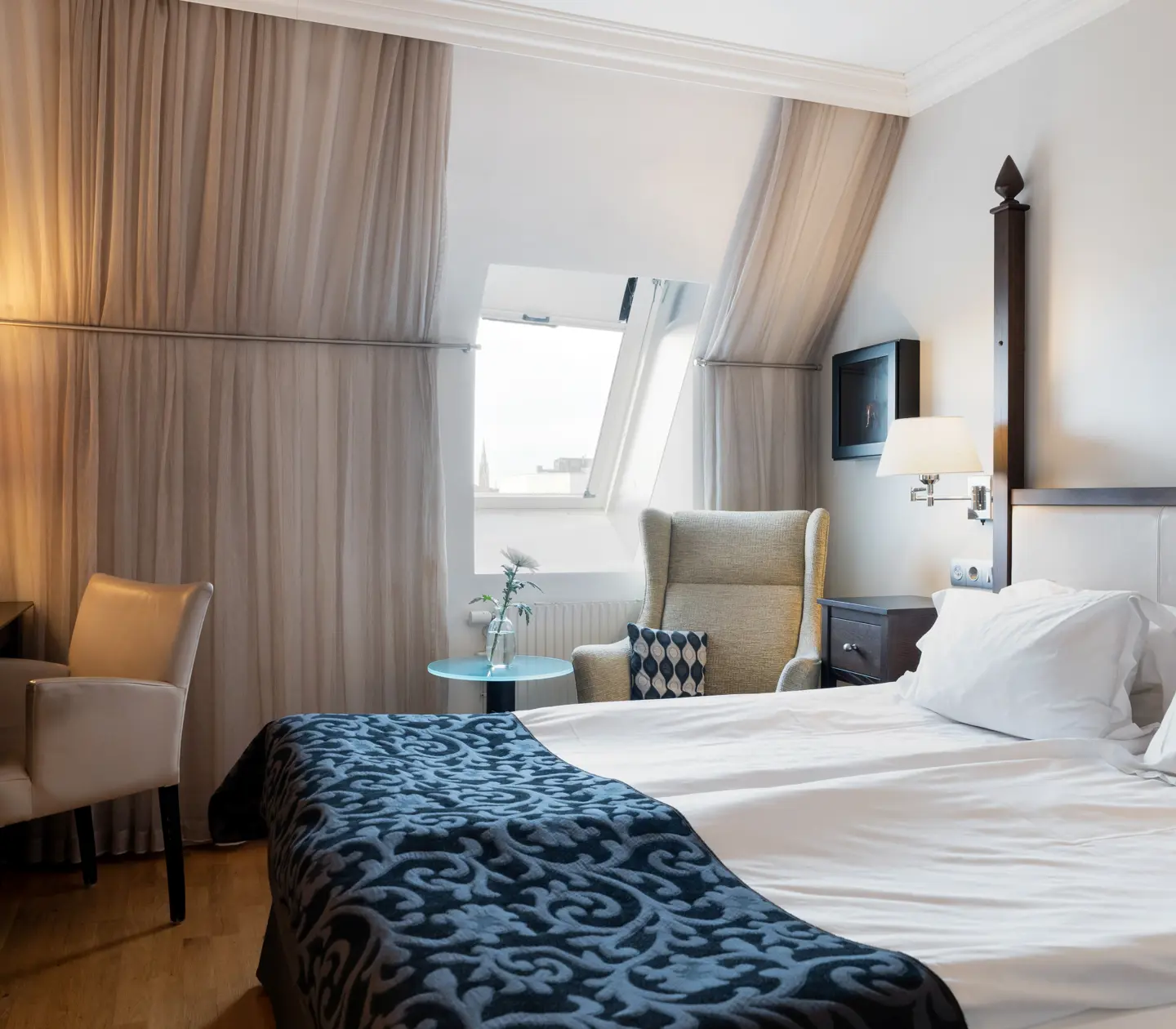 Ljust hotellrum med säng, skrivbord och snedtak