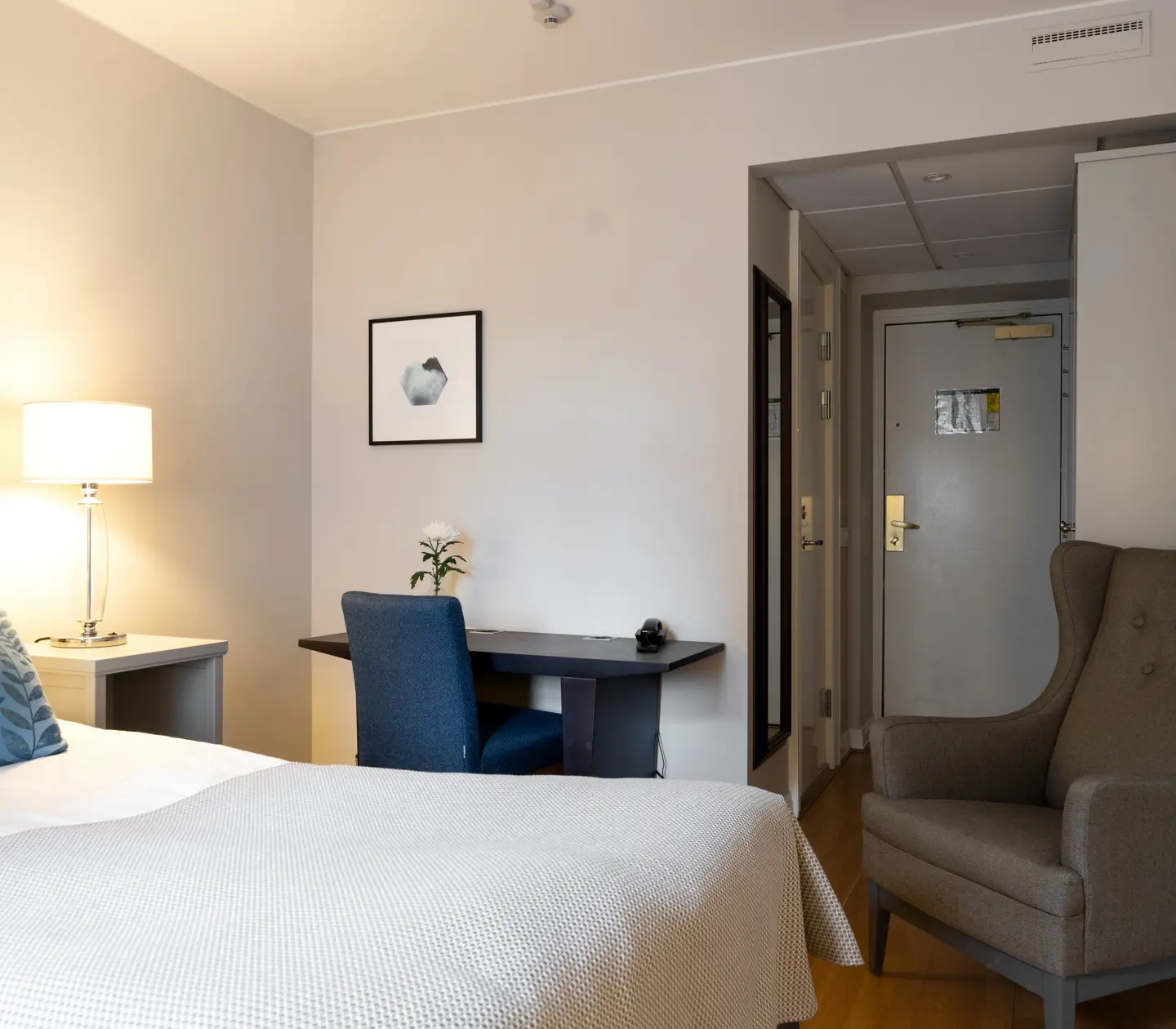 Ljust hotellrum med säng, fåtölj och skrivbord