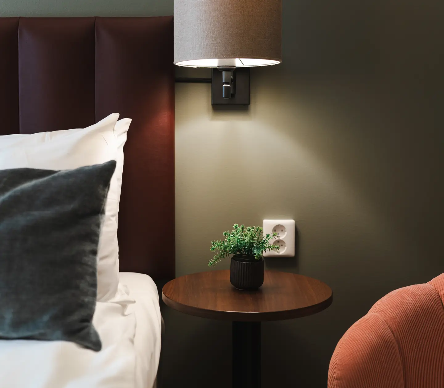 Närbild på hotellrum med säng, sänglampa och blomma