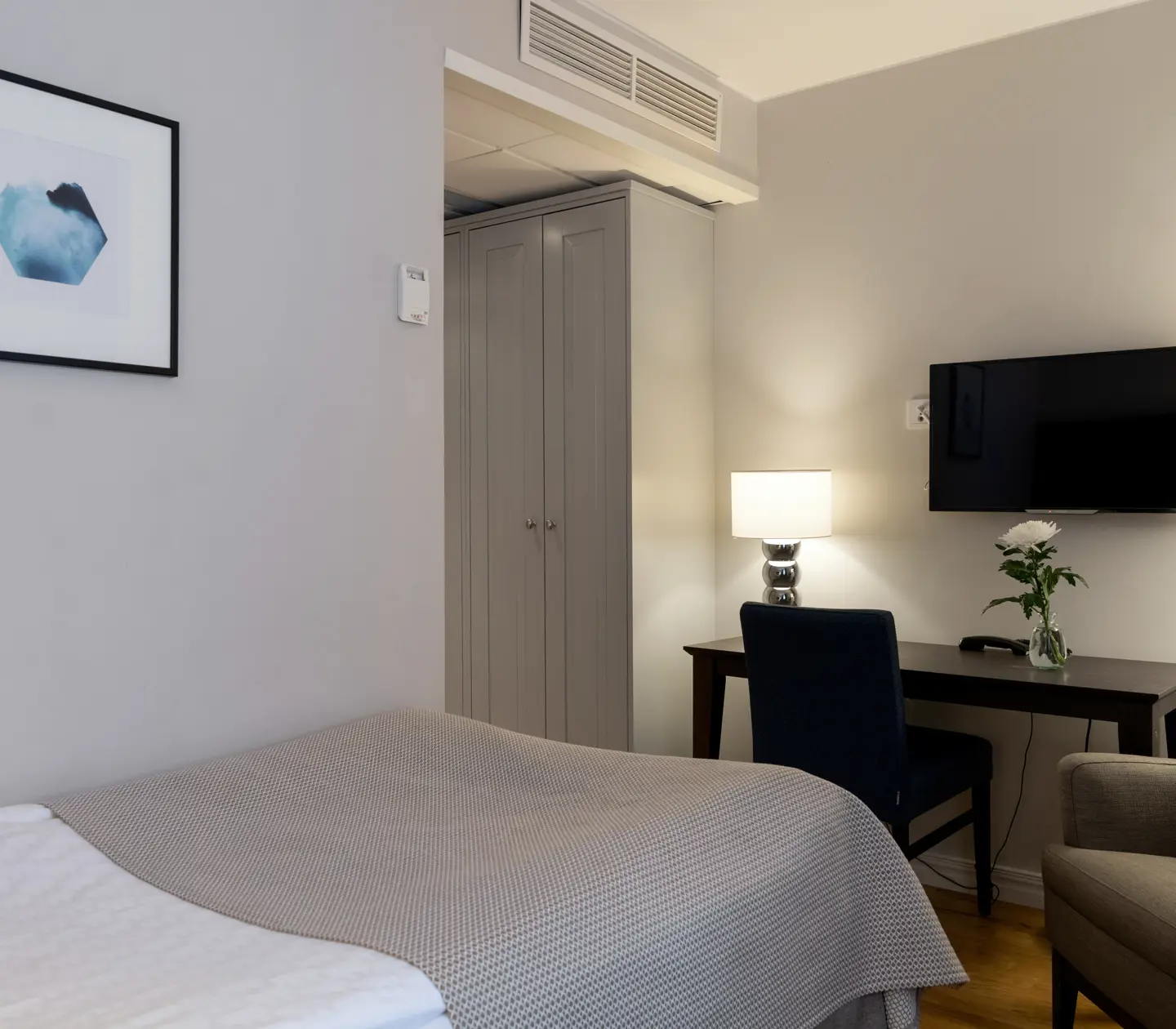 Ljust hotellrum med säng, skrivbord och fåtölj