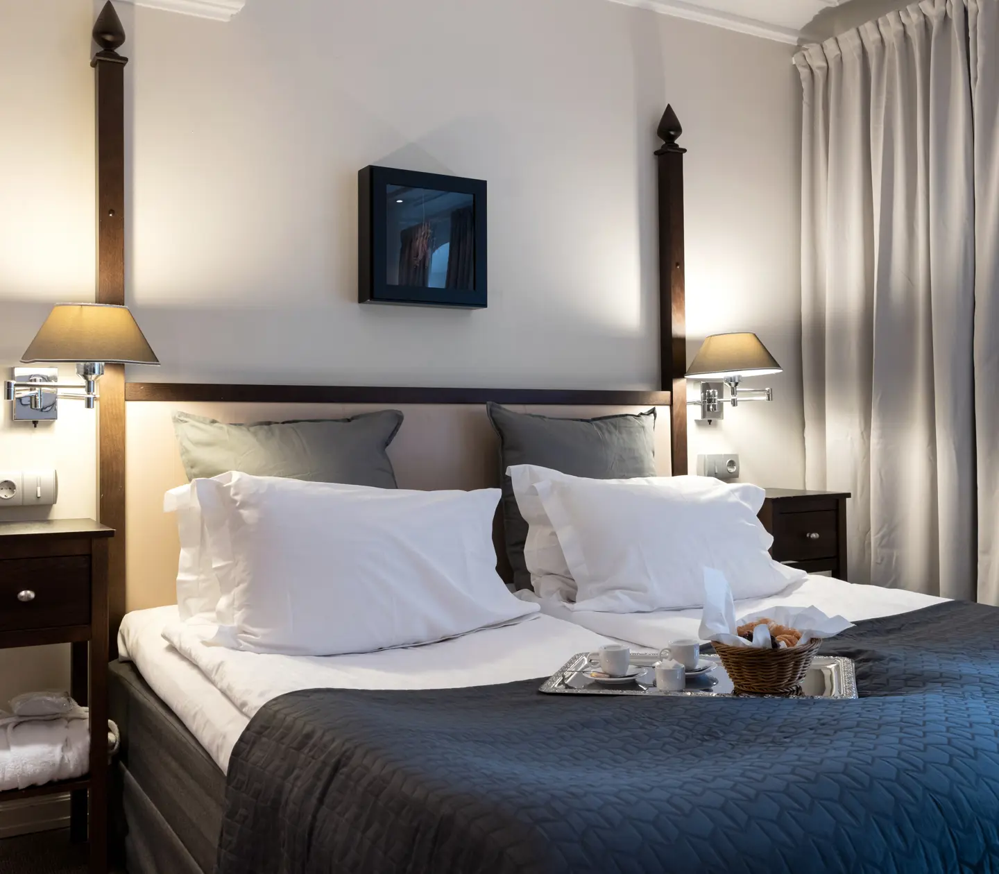Ljust hotellrum med gardiner, säng och nattduksbord