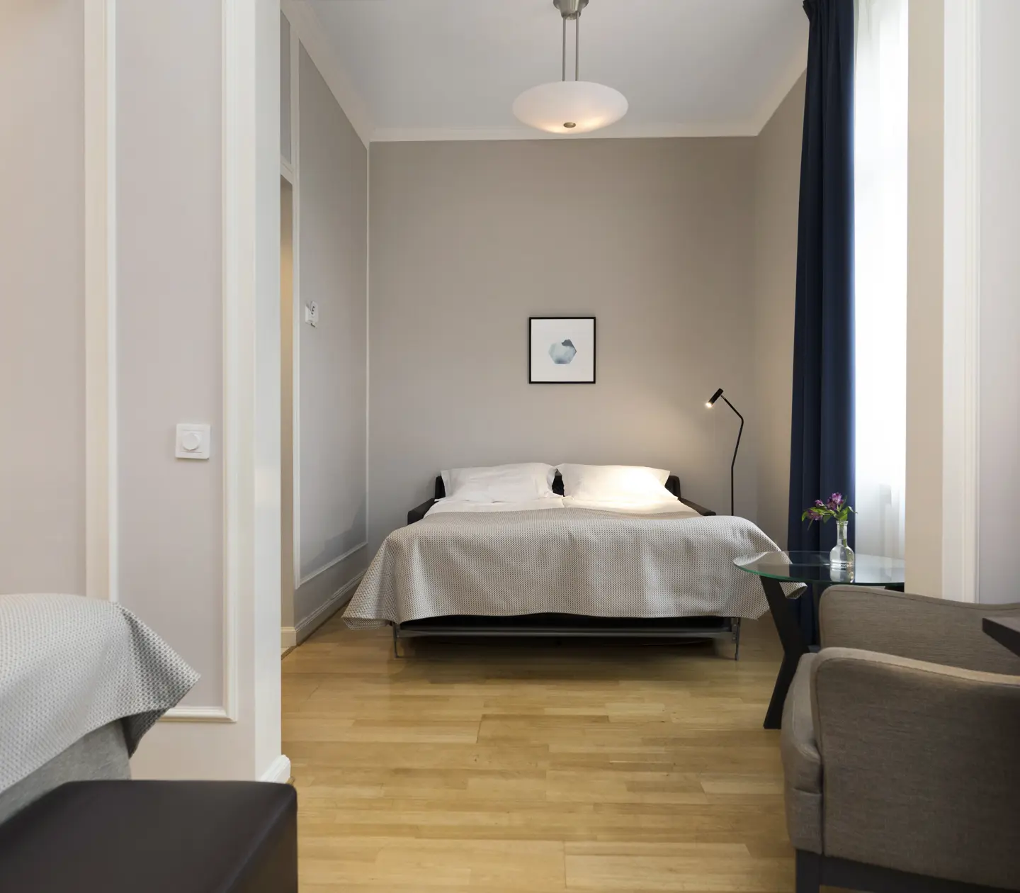 Ljust hotellrum med säng, fåtölj och tavla