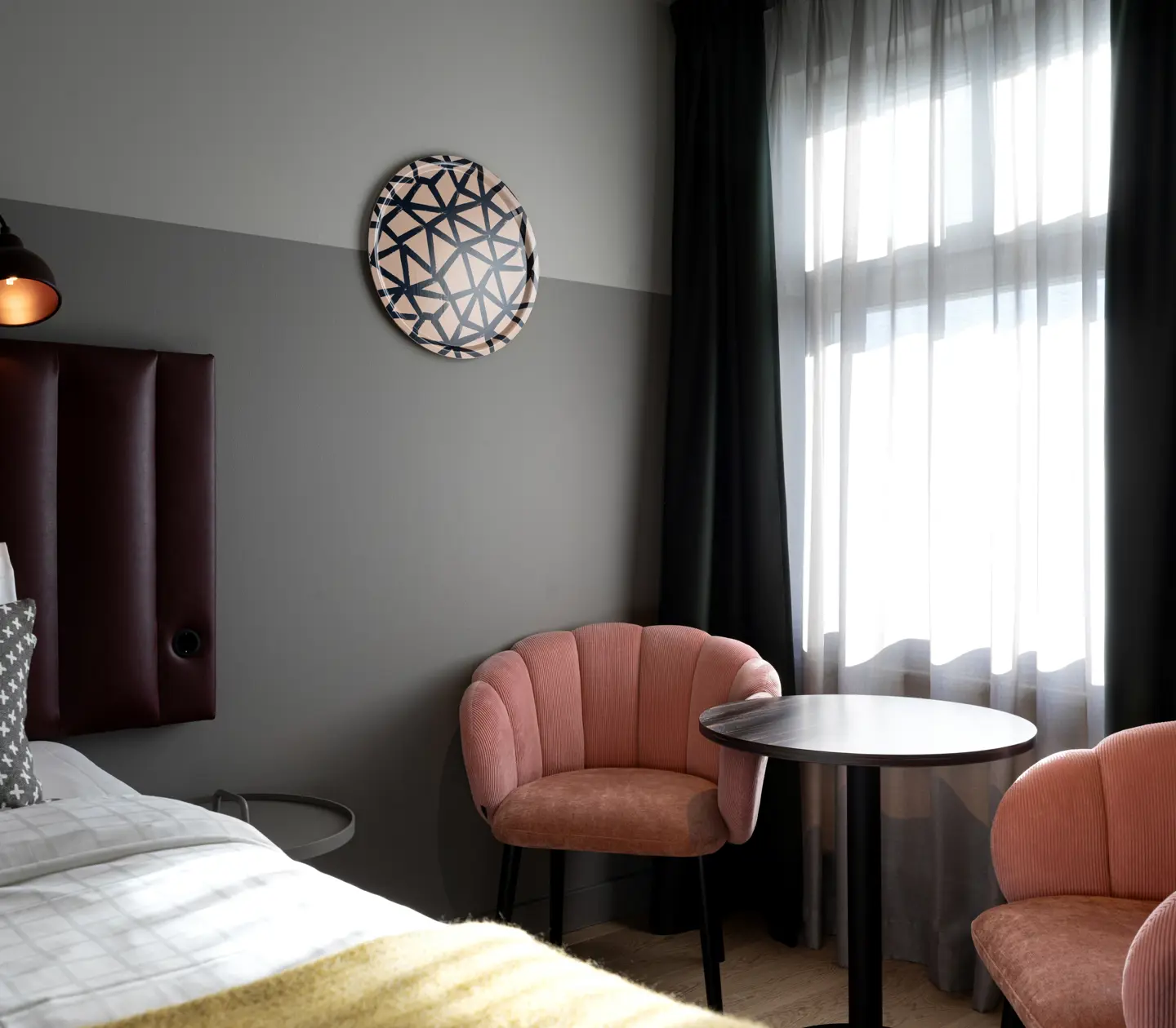 Hotellrum med dubbelsäng, rosa fåtöljer och fönster