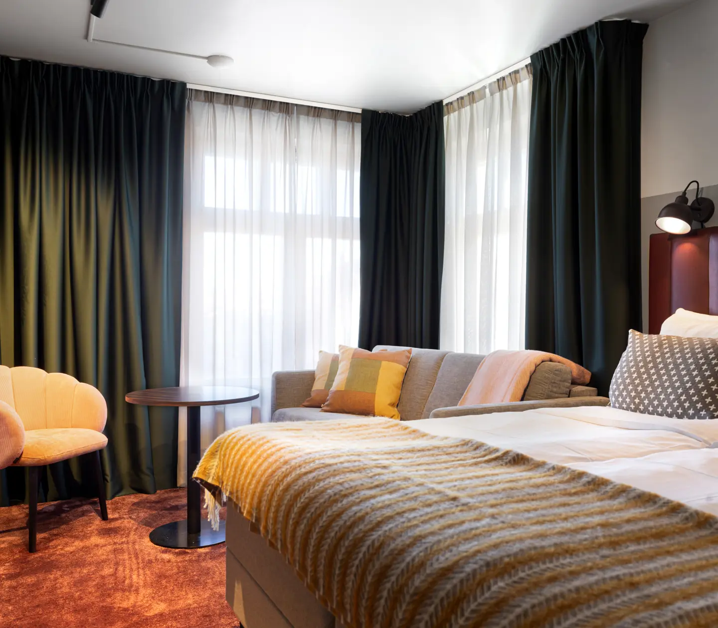 Ombonat hotellrum med dubbelsäng, soffgrupp och gardiner