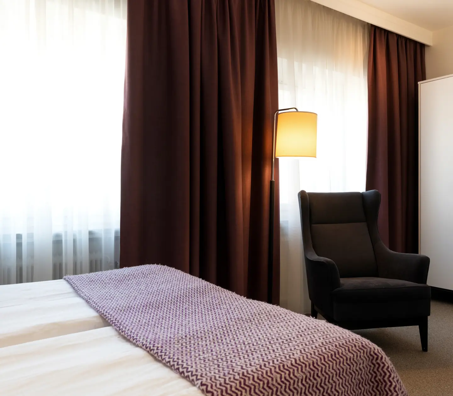 Hotellrum med del av säng, fåtölj, garderob och fönster
