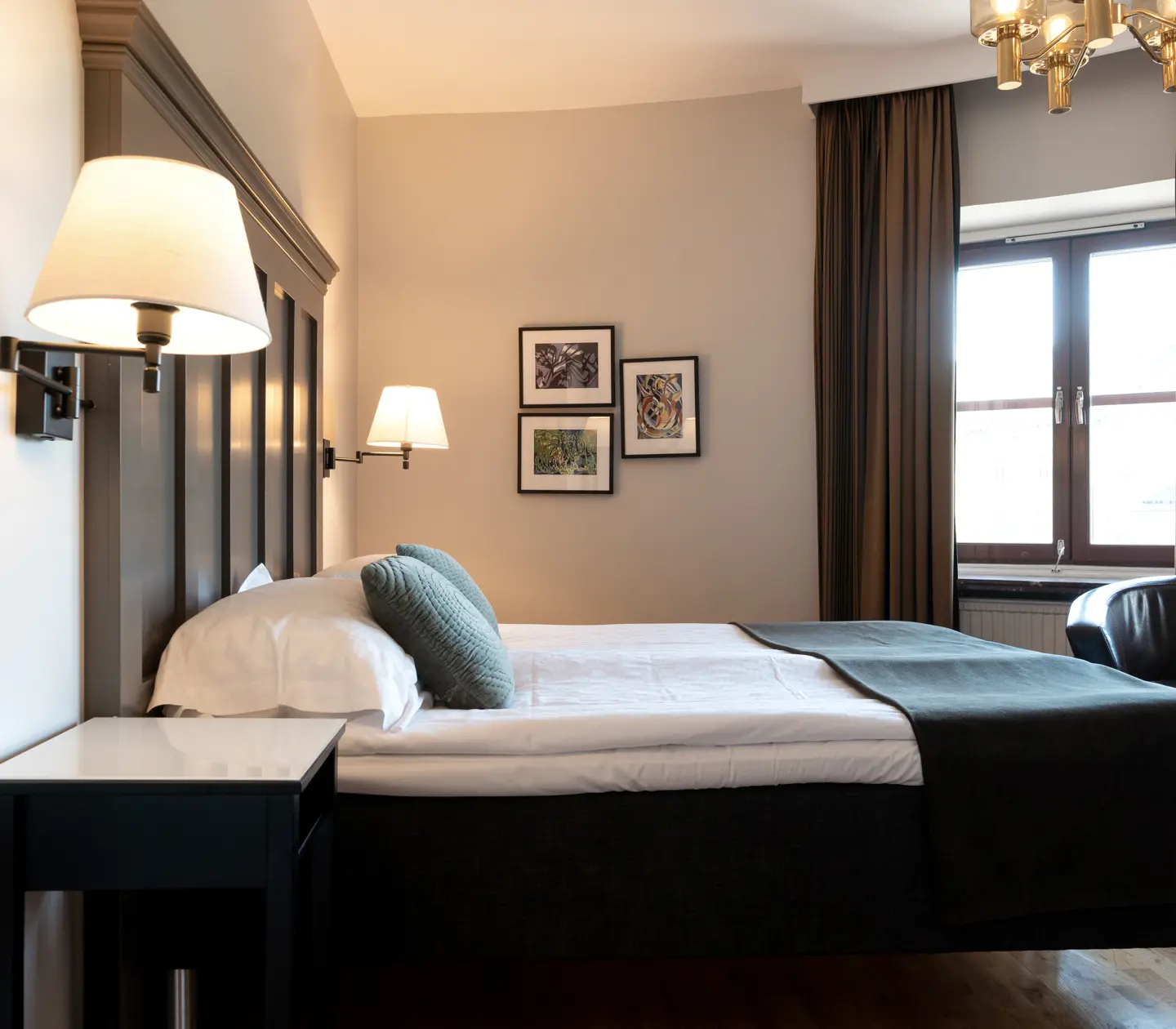Ljust hotellrum med dubbelsäng, fåtölj och fönster