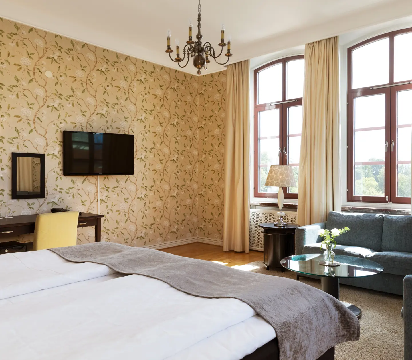 Mysigt hotellrum med blommig tapet, hörnsoffa och stora fönster