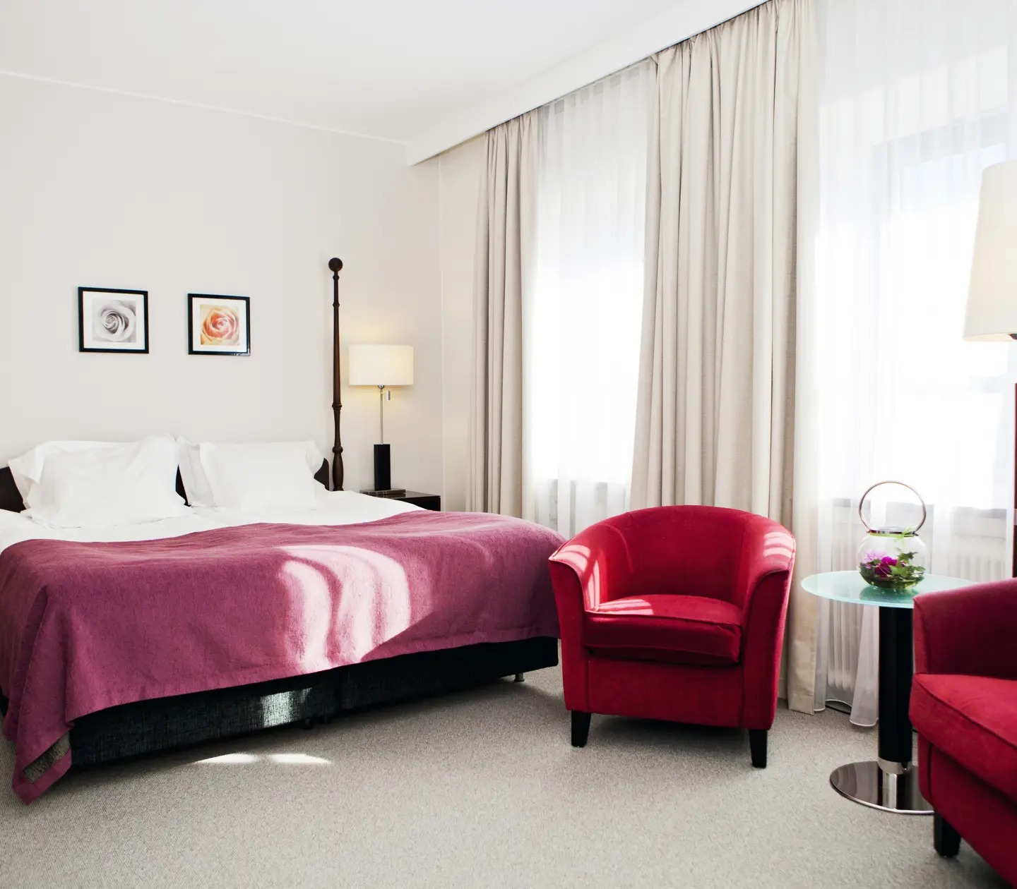 Ljust hotellrum med dubbelsäng, fåtöljer och fönster