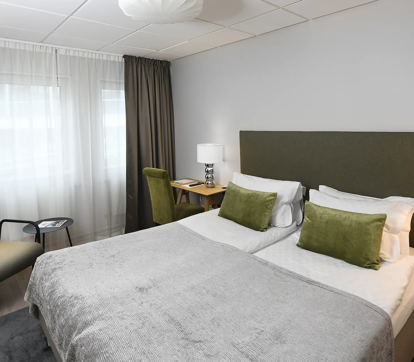 Ljust hotellrum med dubbelsäng, skrivbord, fåtölj och fönster
