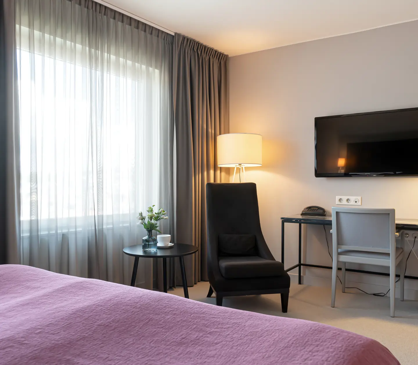 Hotellrum med dubbelsäng, skrivbord, fåtölj och fönster