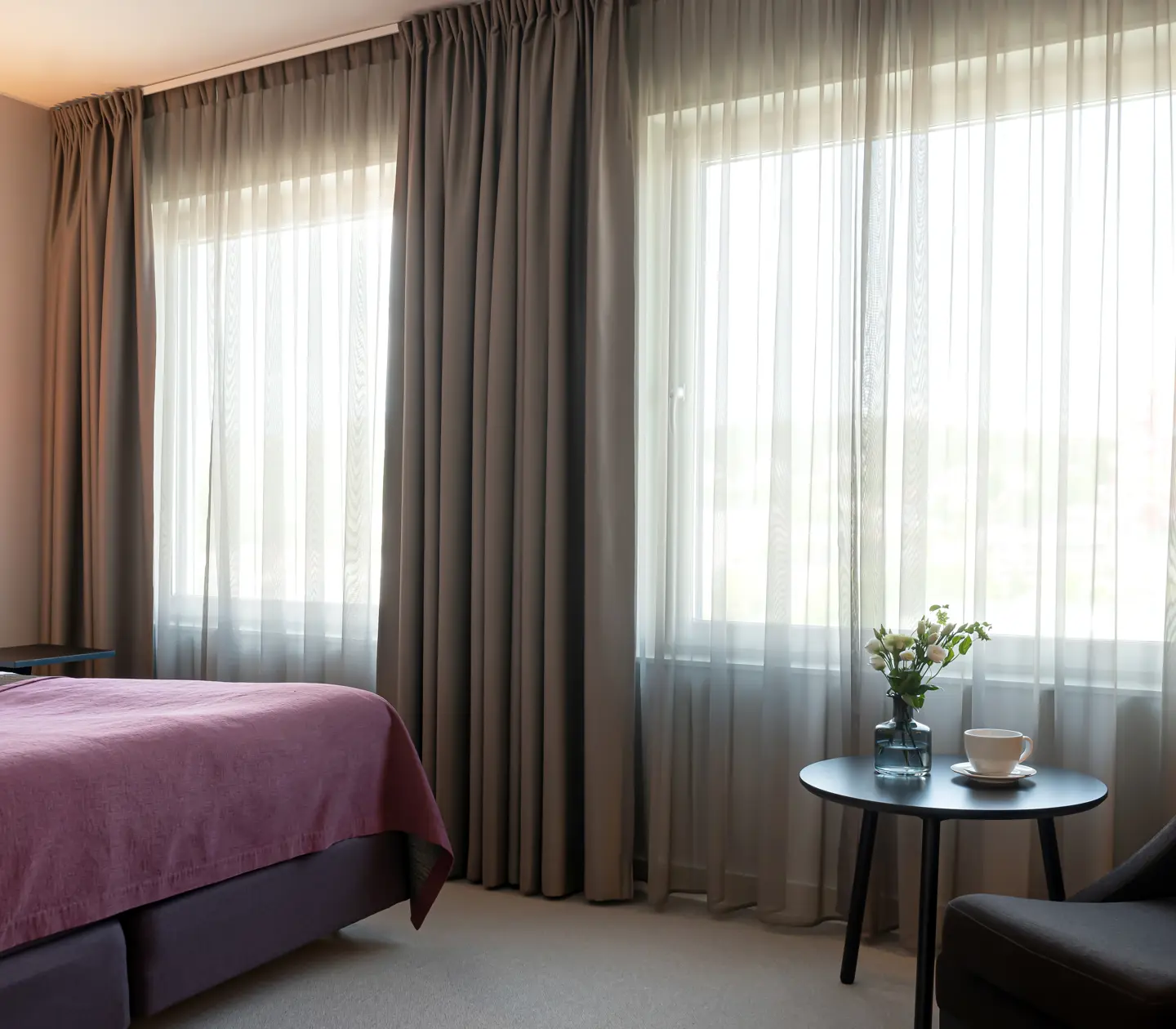 Hotellrum med dubbelsäng, fåtölj och stora fönster