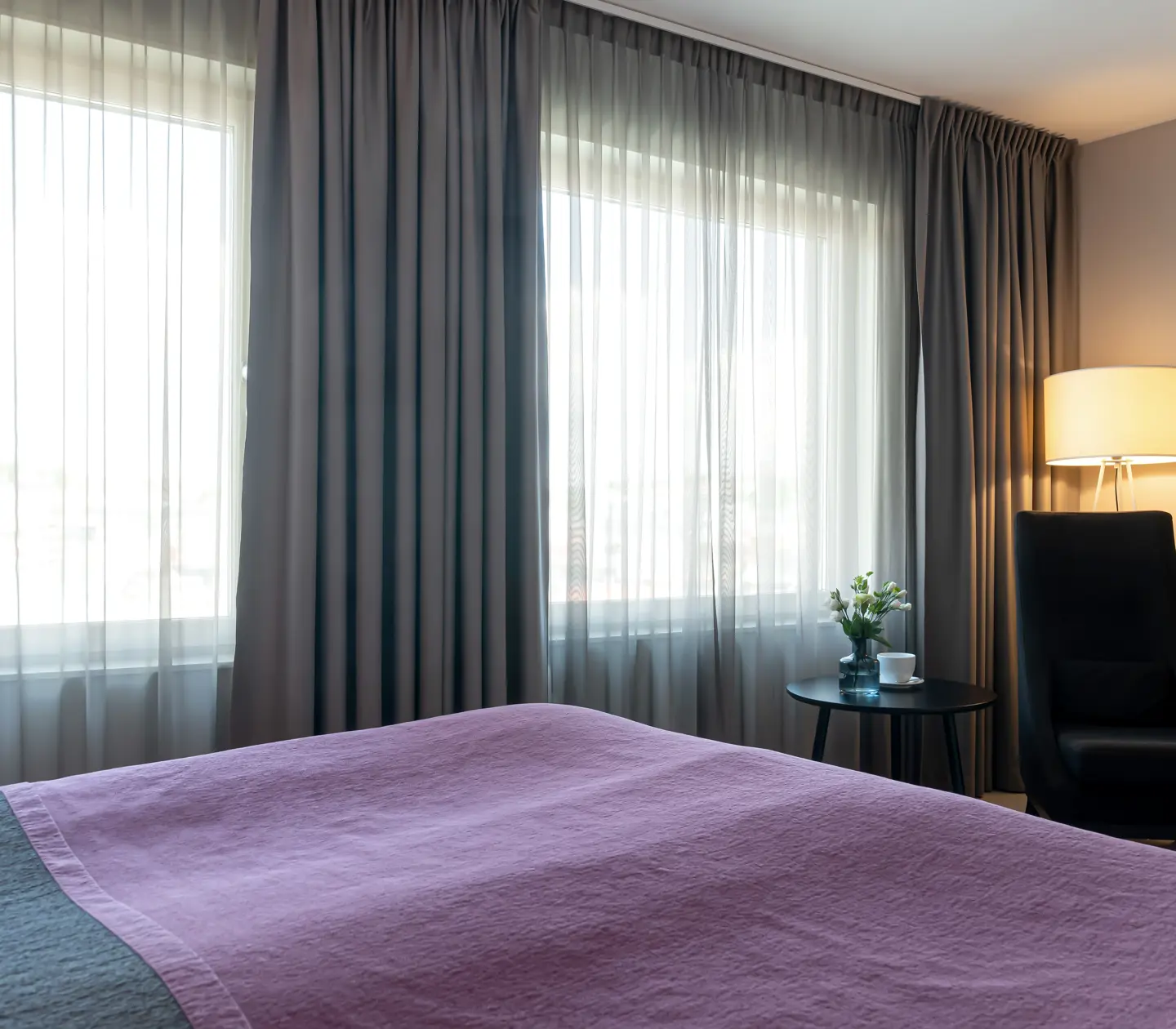 Hotellrum med dubbelsäng, fåtölj och stora fönster