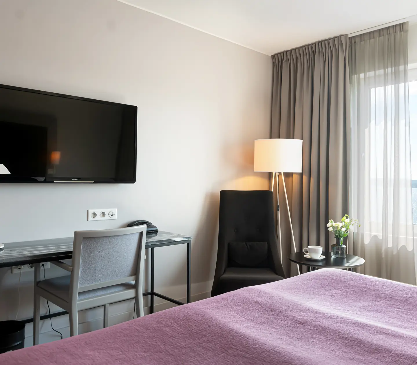 Hotellrum med skrivbord, tv, fåtölj och fönster