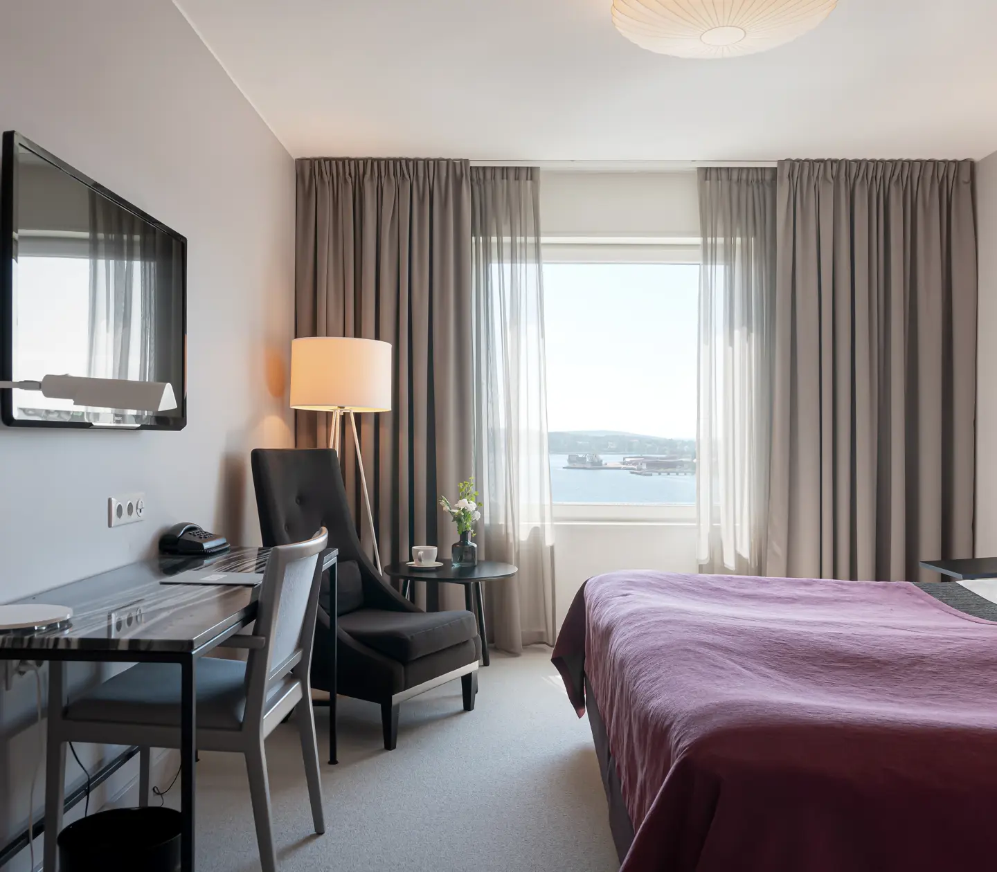 Hotellrum med dubbelsäng, skrivbord, fåtölj och fönster