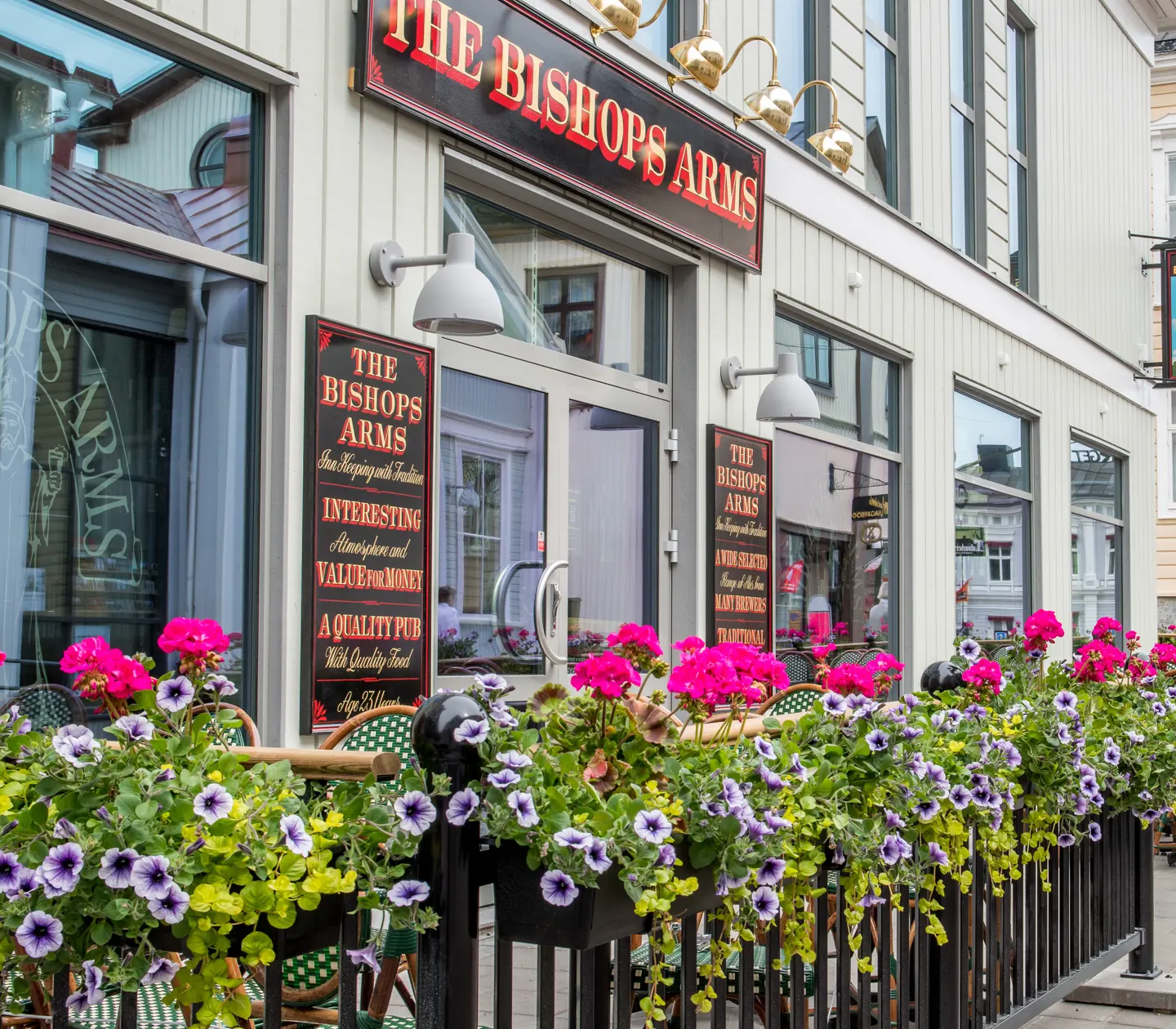 Uteservering för The Bishops Arms med blommor, skyltar och matgrupper