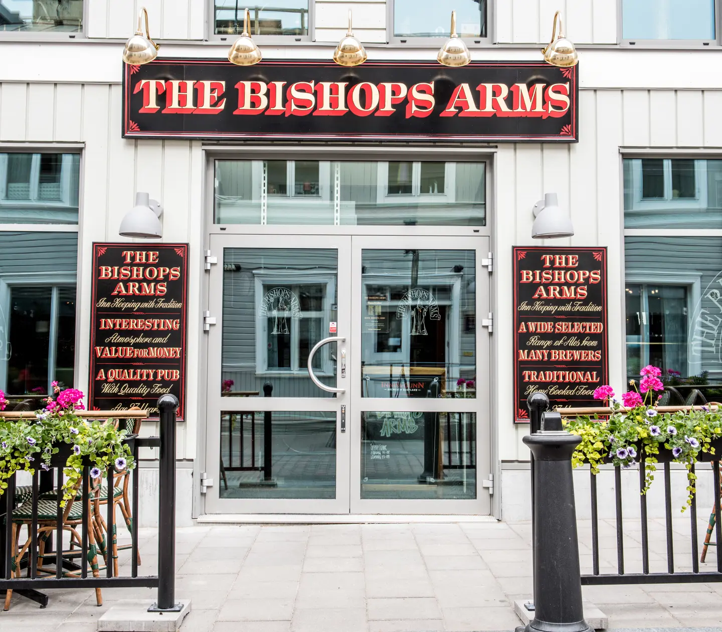 Entré till The Bishops Arms med stora glasdörrar, blommor och skyltar