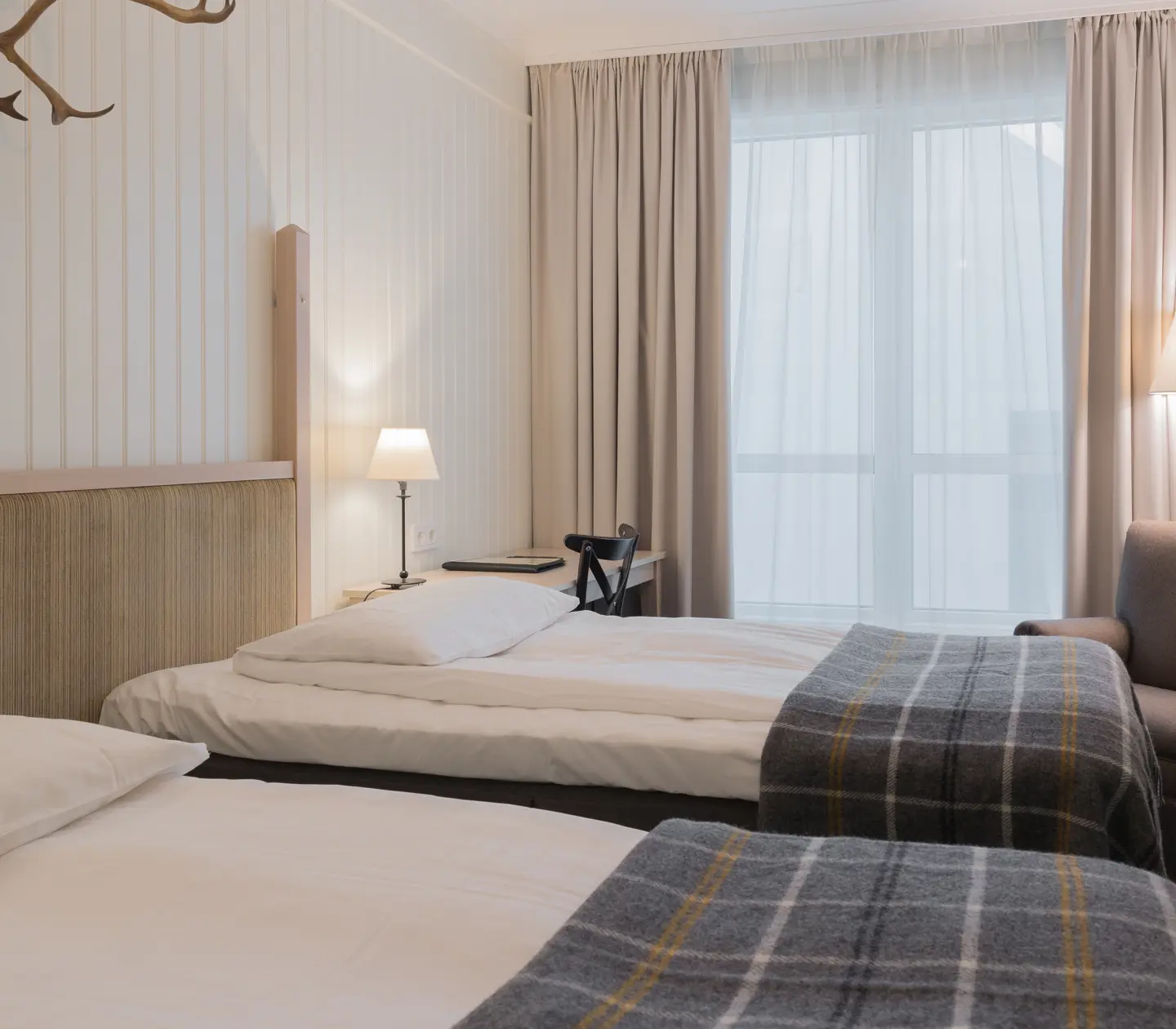 Mysigt hotellrum med separerade sängar, fönster och fåtölj