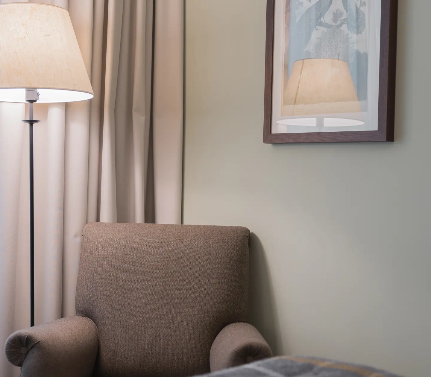 Hotellrum med fåtölj, golvlampa och tavla