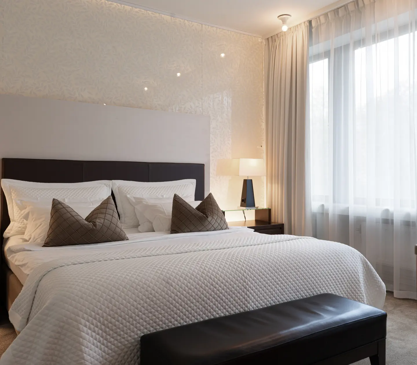 Elegant hotellrum med en stor säng, vita sängkläder och dekorativa kuddar.