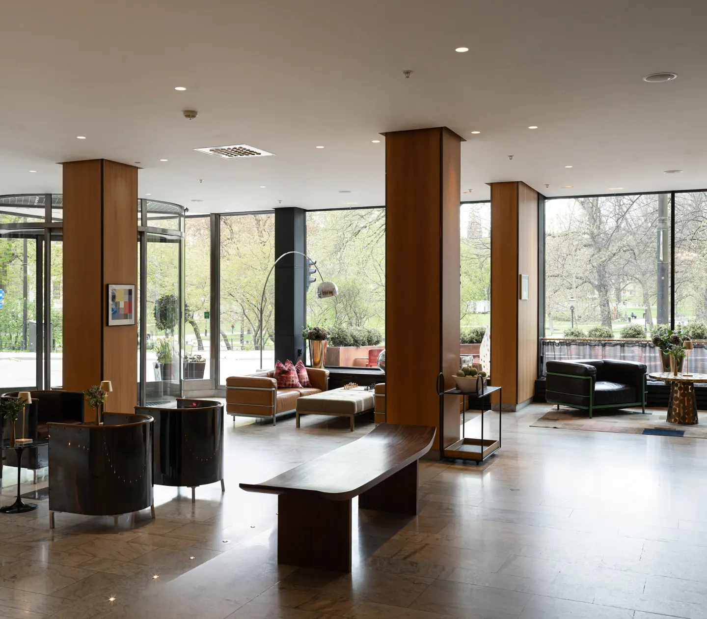 Modern hotelobby med bekväma sittplatser, naturligt ljus från stora fönster och utsikt över en grön park.