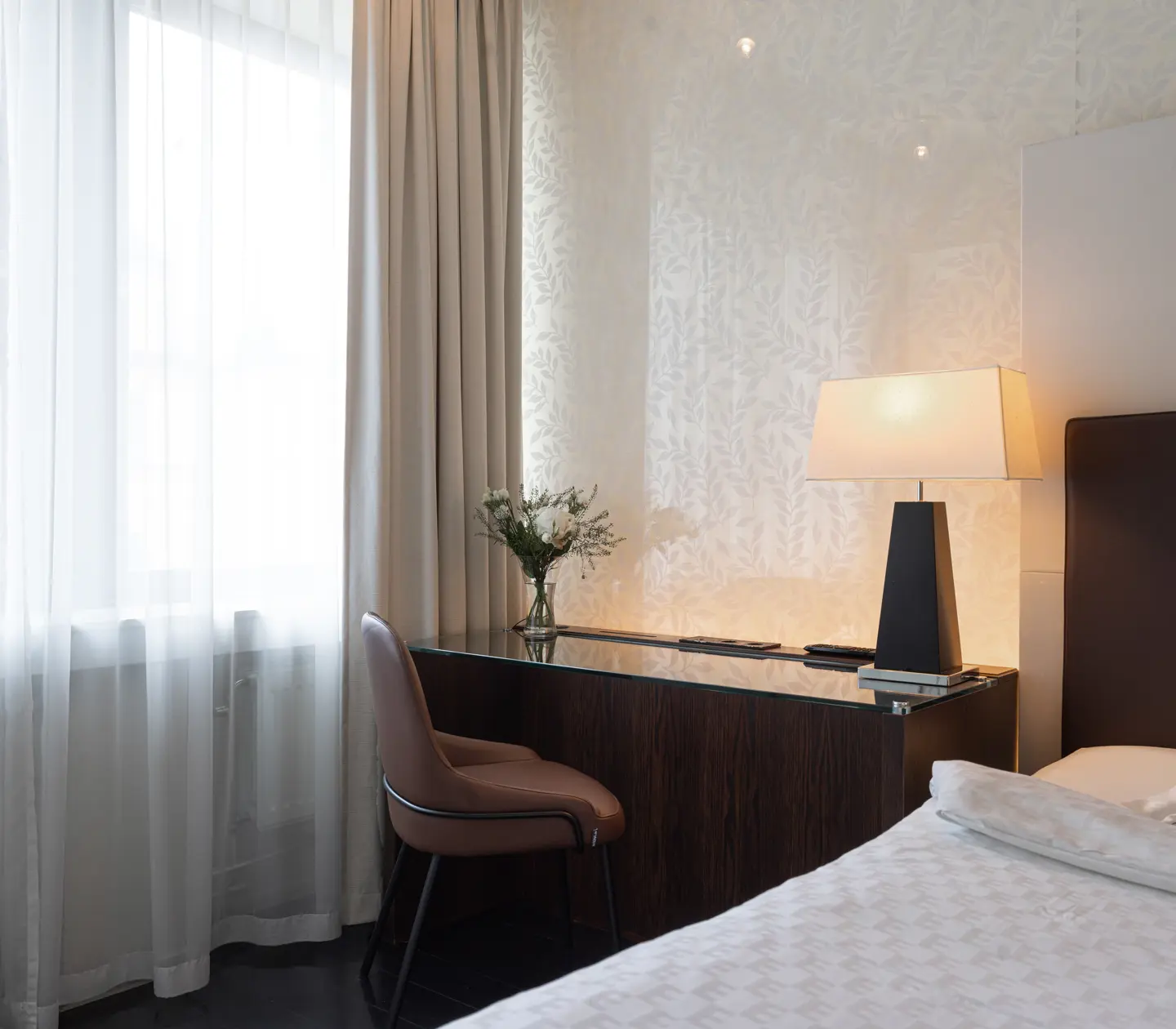 Ljust hotellrum med säng, skrivbord och fönster