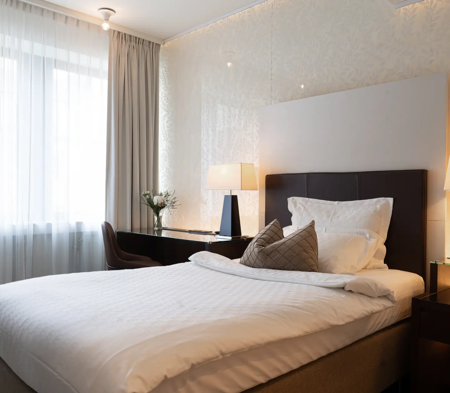 Ljust hotellrum med säng, skrivbord och fönster