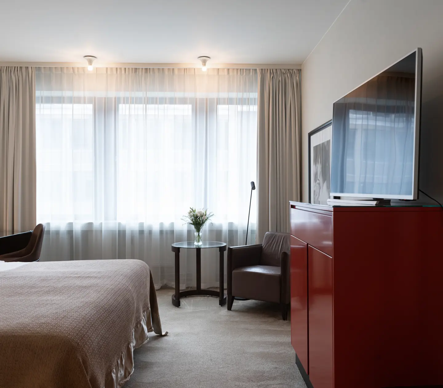 Ljust hotellrum med säng, tv, skrivbord och fönster