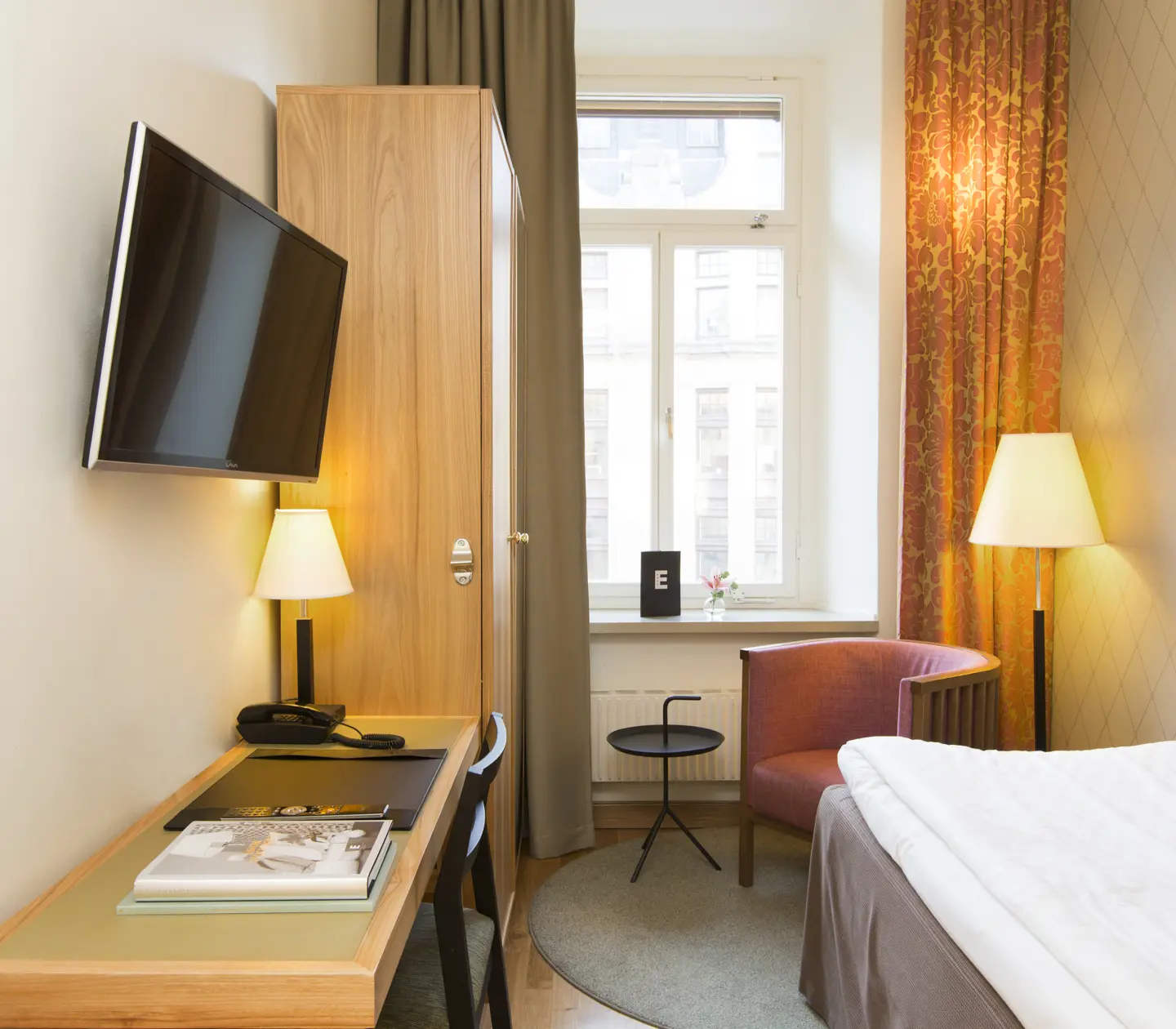 Hotellrum med enkelsäng, skrivbord och fåtölj