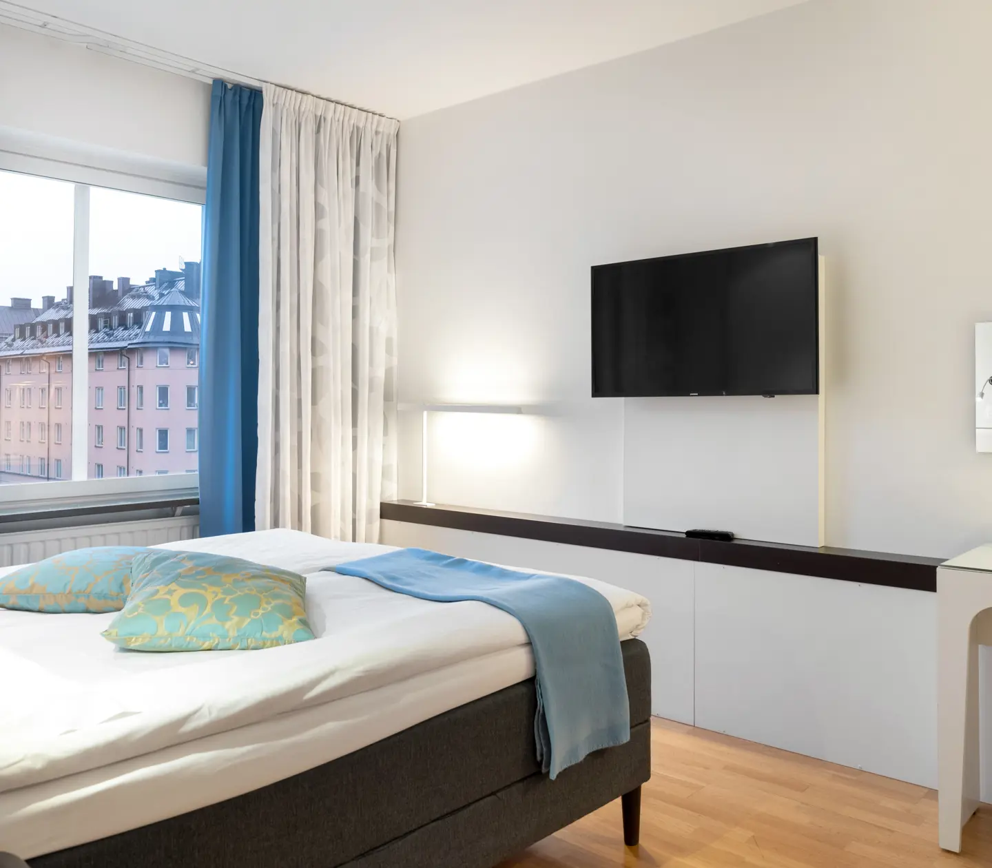 Ljust hotellrum med säng, skrivbord och tv