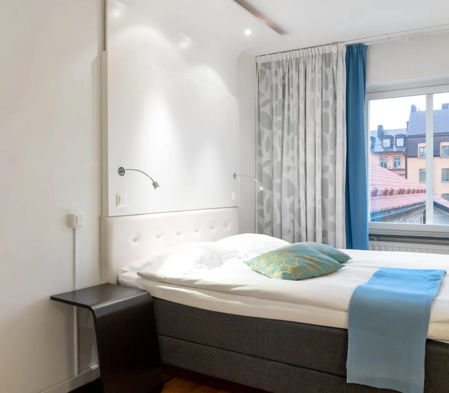 Ljust hotellrum med säng, fönster och blå textilier