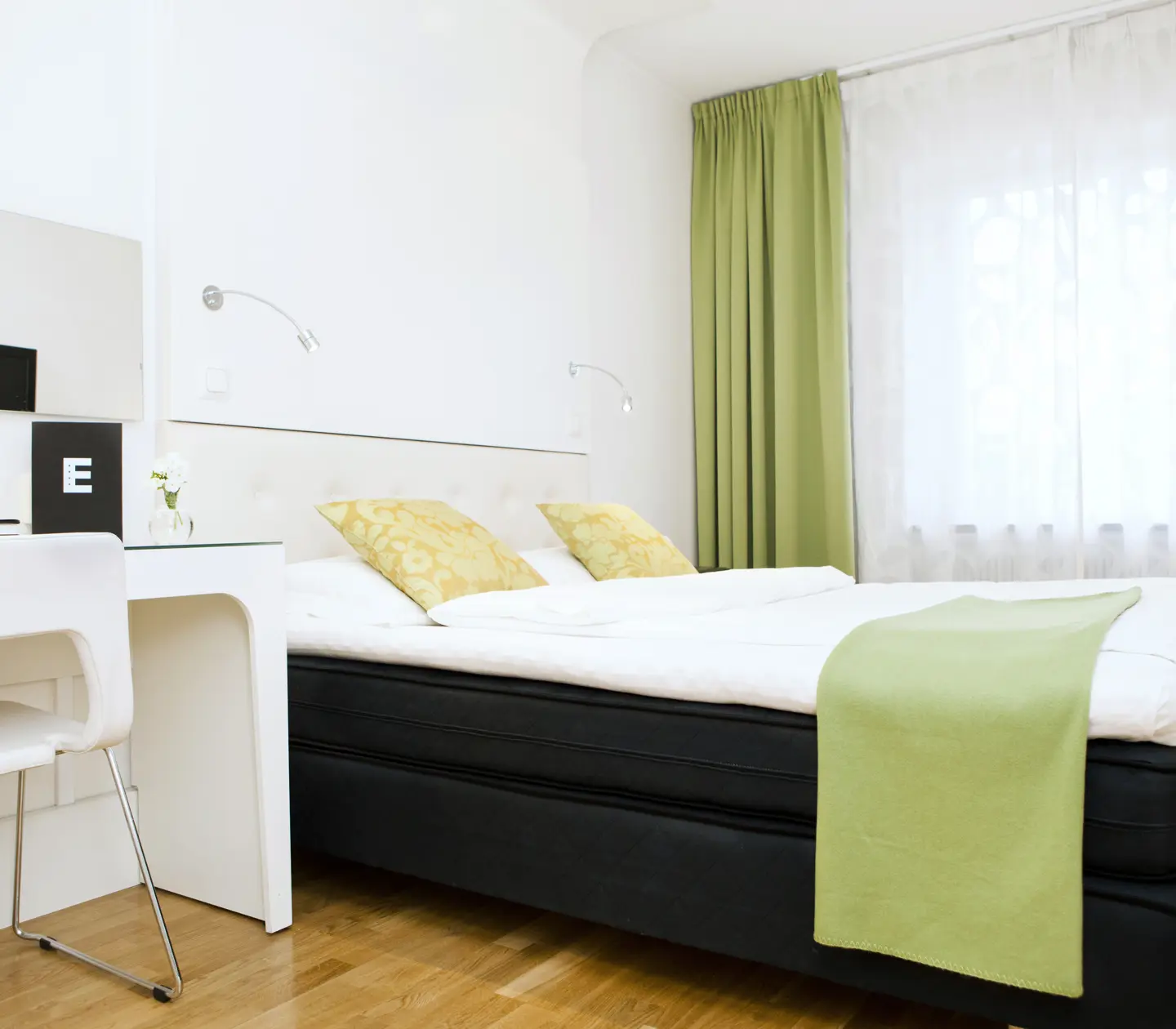 Ljust hotellrum med säng, skrivbord och gröna textilier