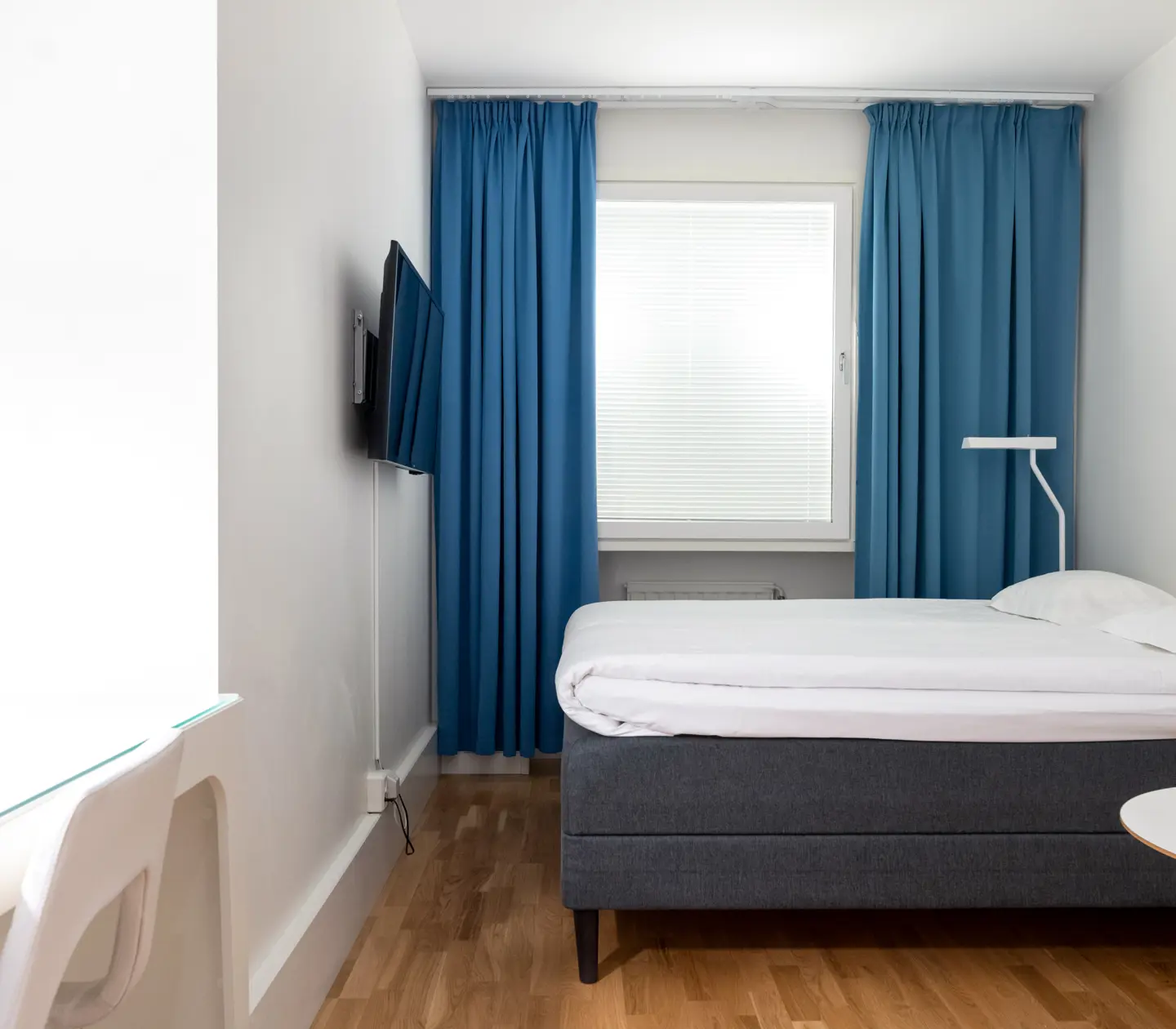 Ljust hotellrum med säng, blå textilier och skrivbord