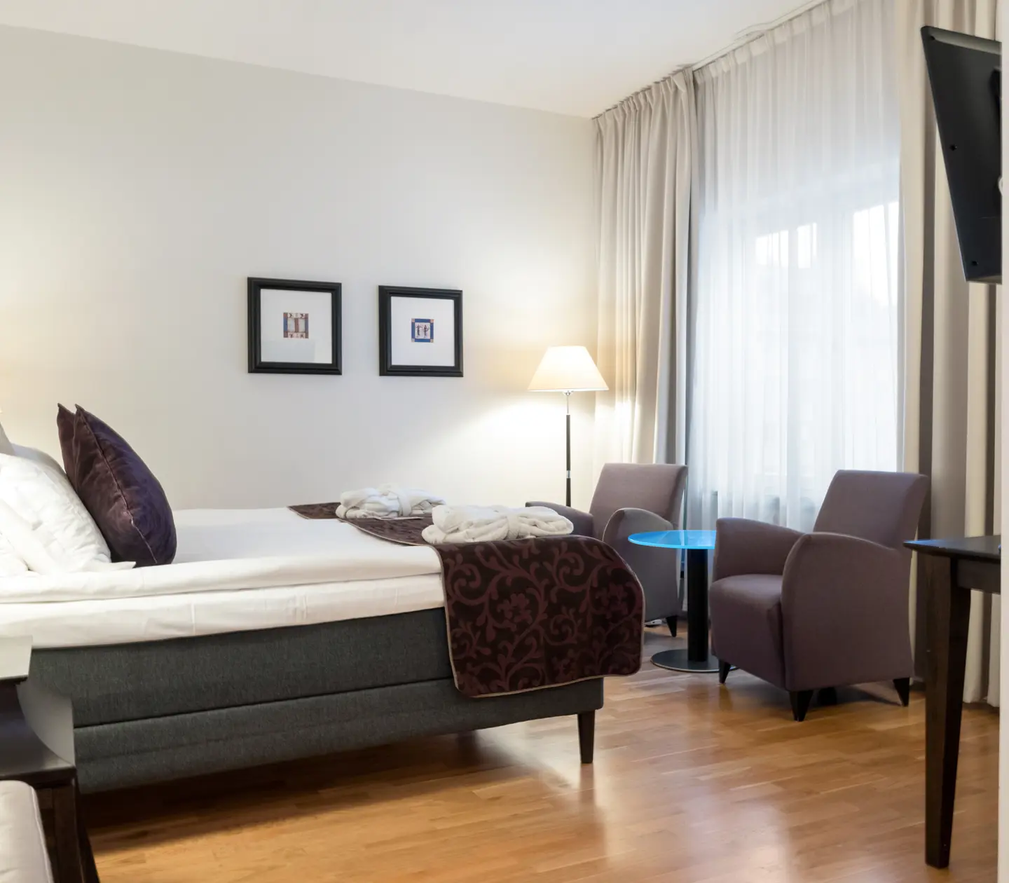 Ljust hotellrum med säng, tavlor och fåtöljer