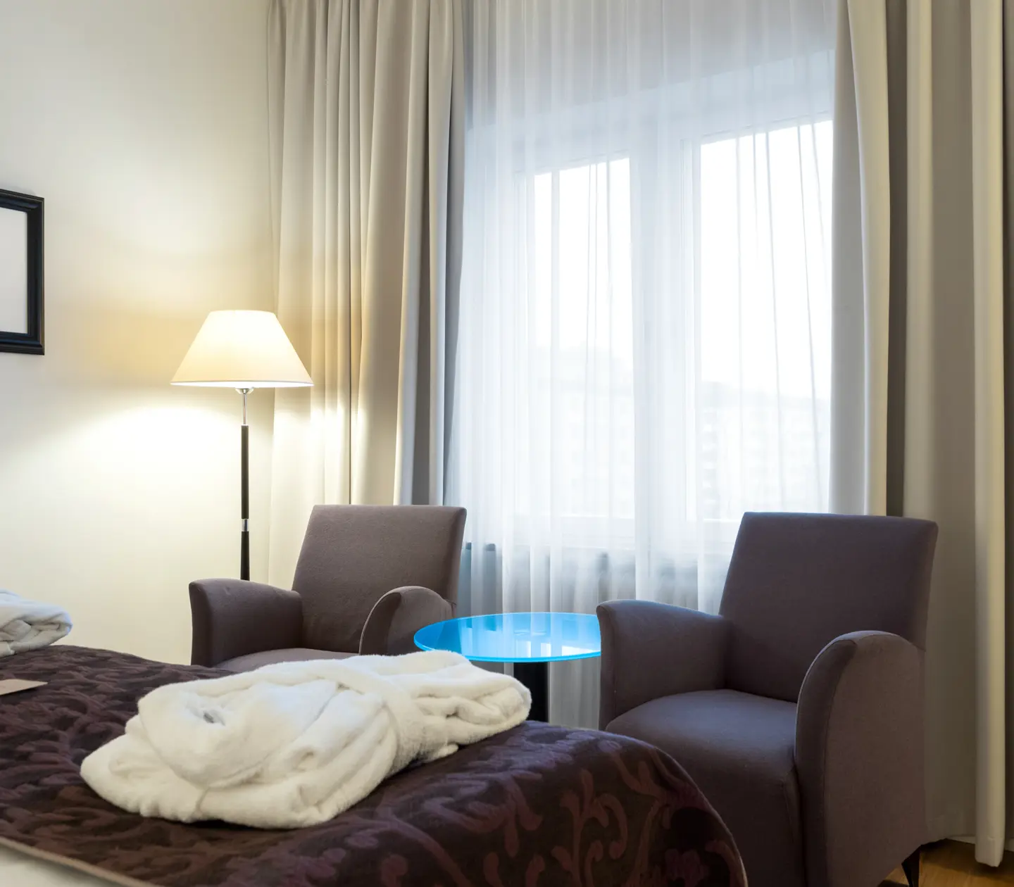 Ljust hotellrum med säng, fåtöljer och gardiner