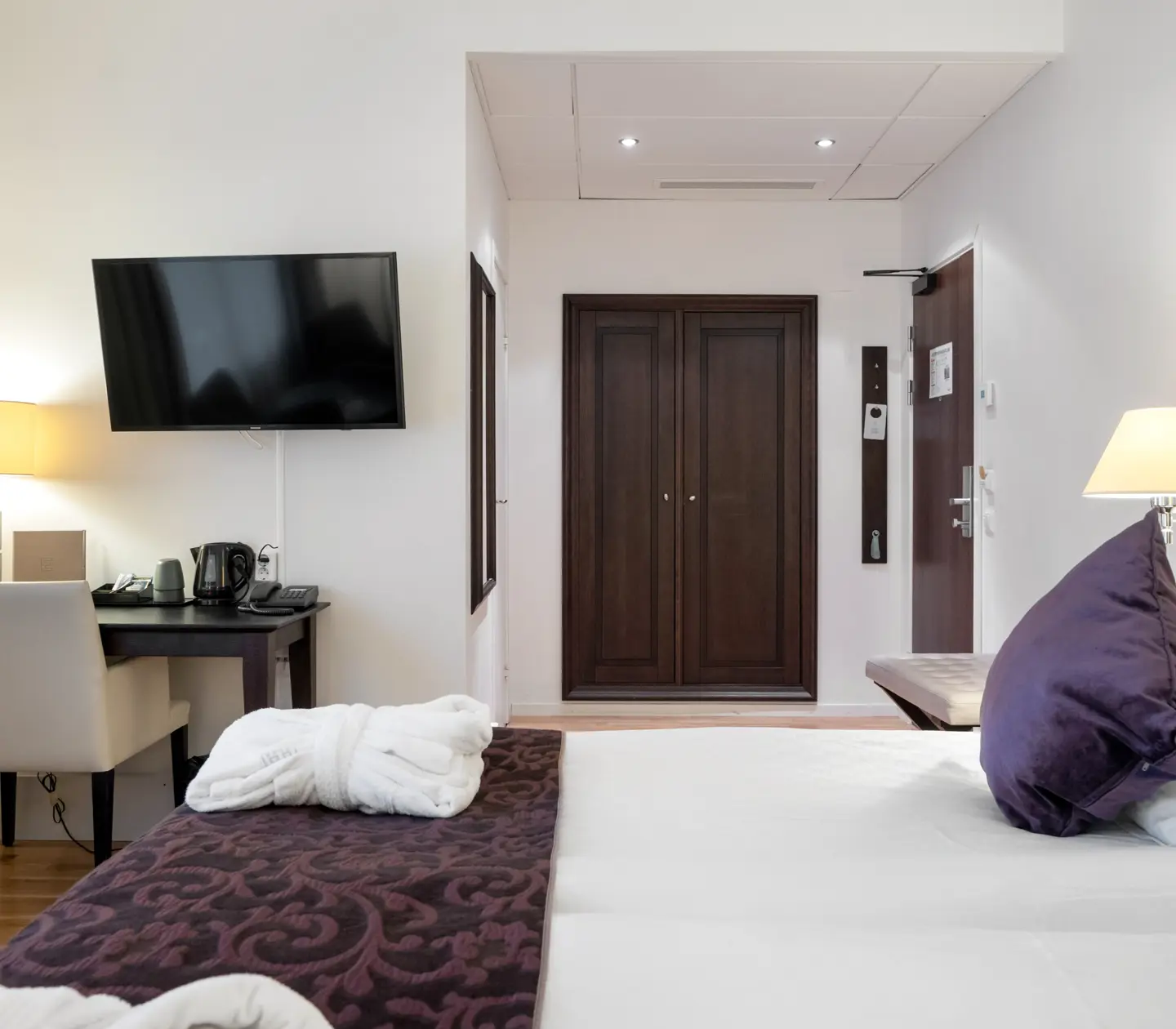 Ljust hotellrum med säng, tv och skrivbord