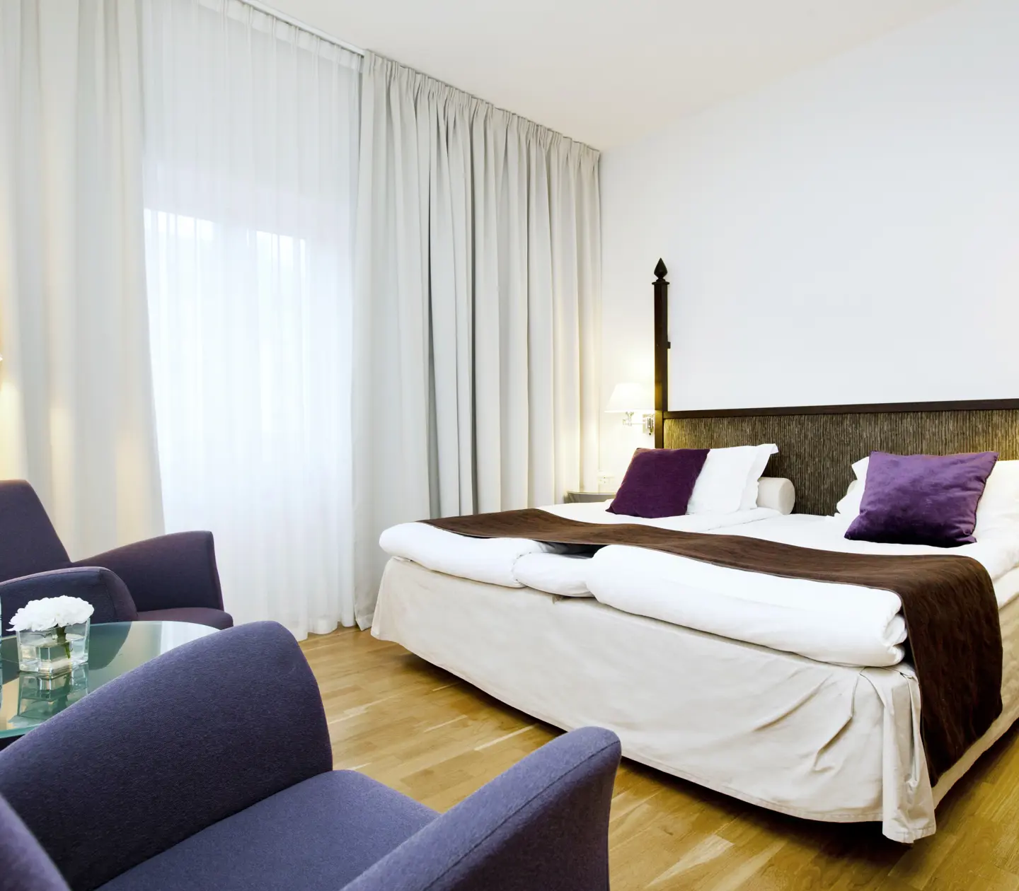 Ljust hotellrum med säng, fåtöljer och gardiner