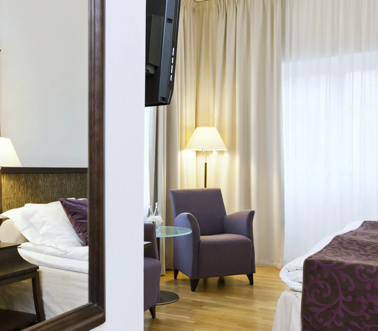 Ljust hotellrum med säng, spegel och fåtöljer