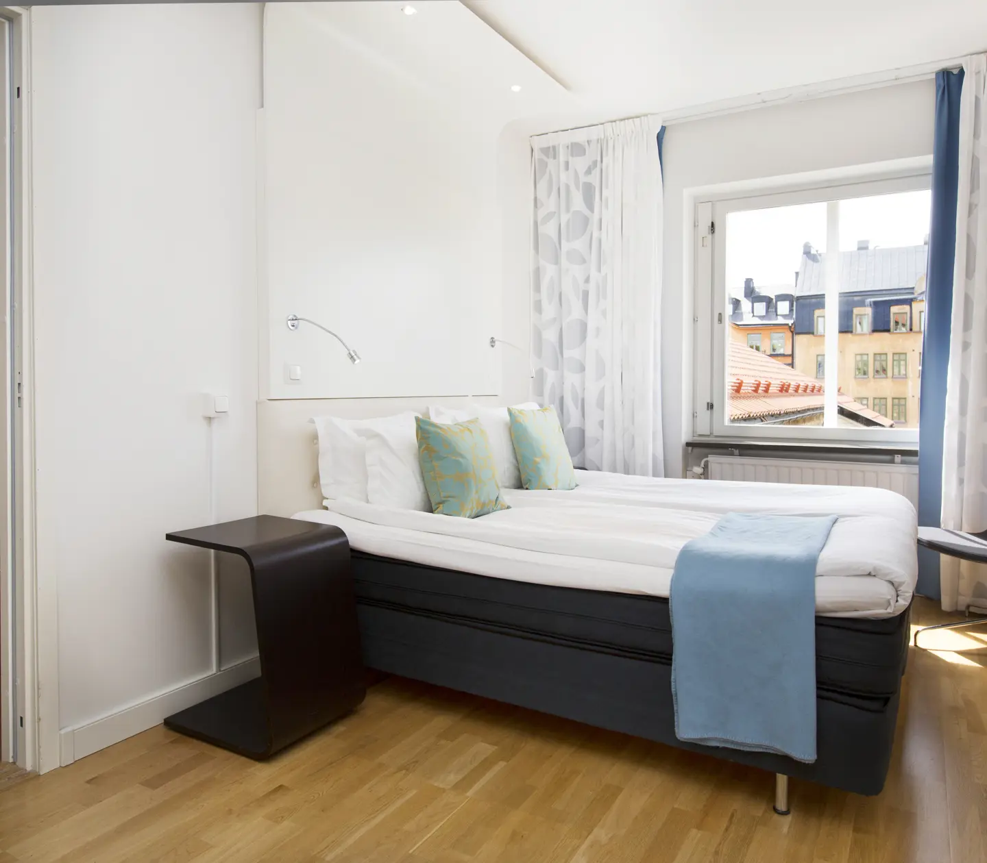 Ljust hotellrum med säng, blå textilier och fåtöljer