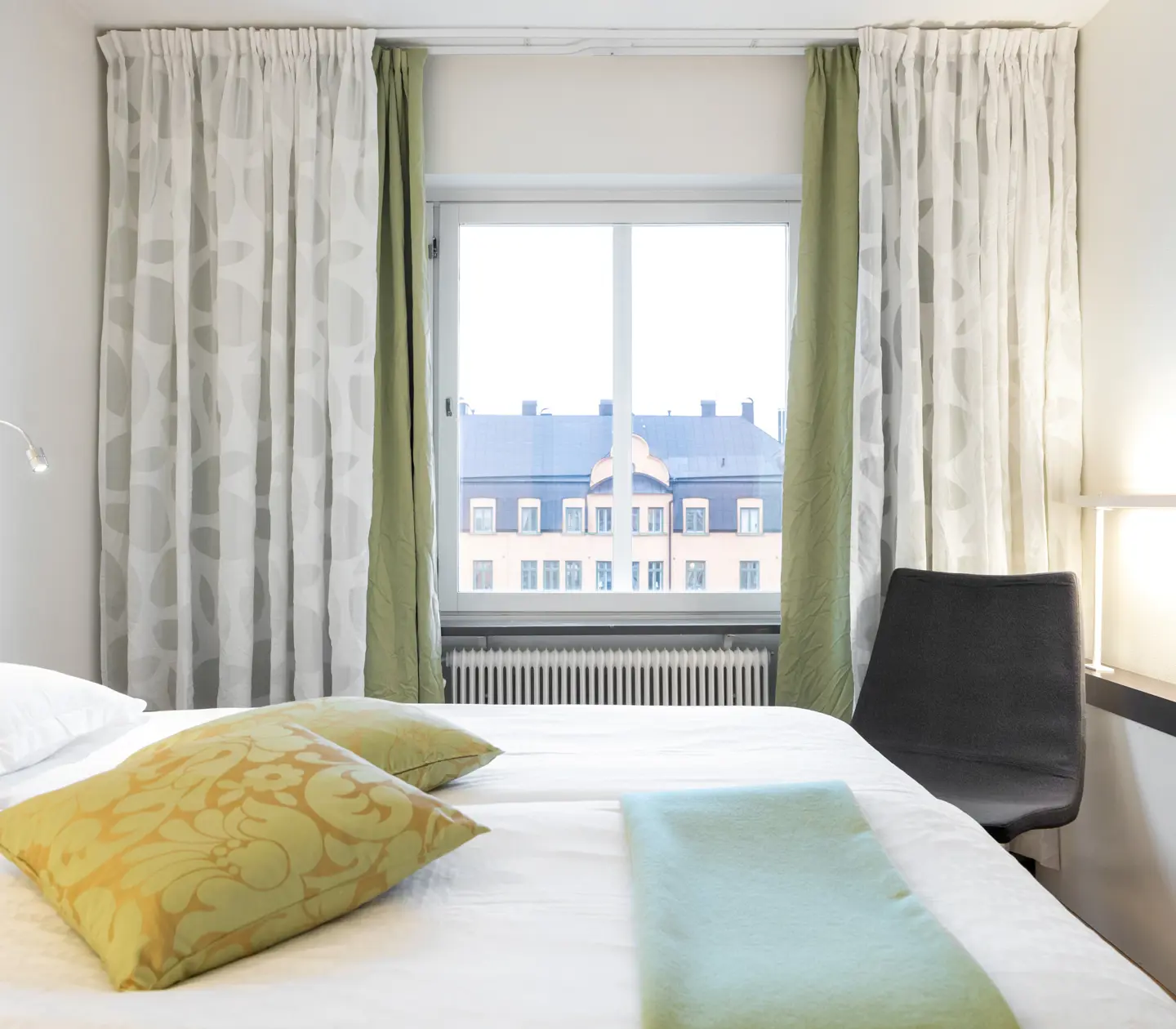 Ljust hotellrum med säng, stol och fönster