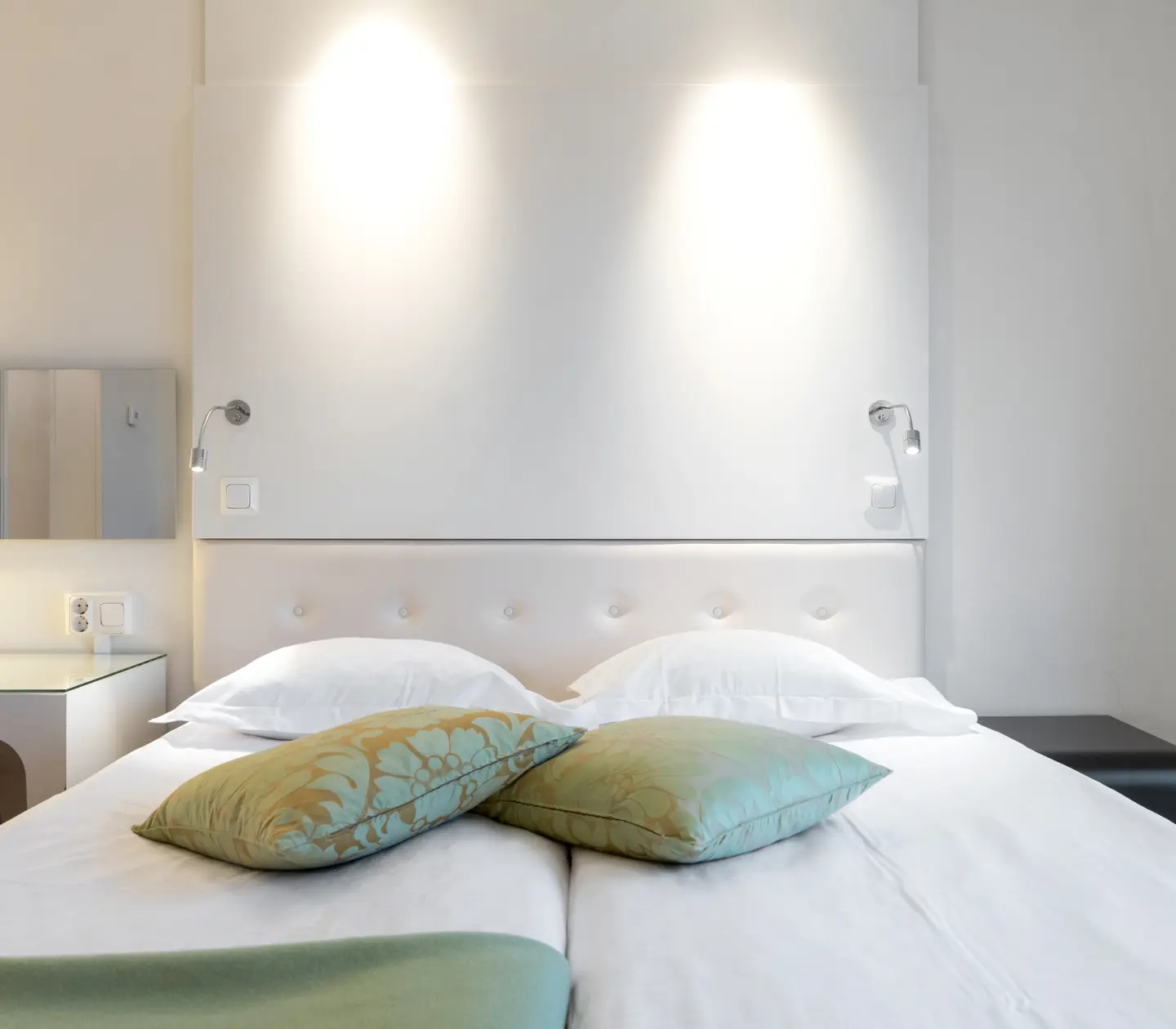 Ljust hotellrum med säng, gröna textilier och skrivbord