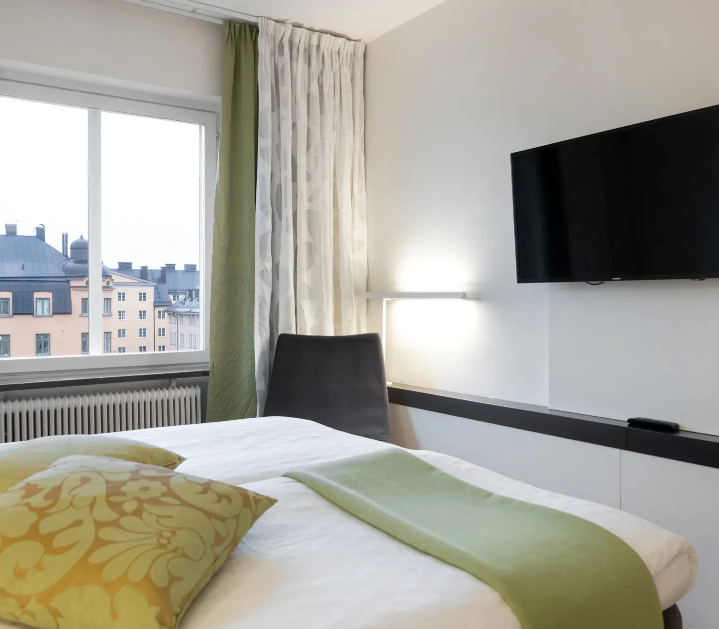 Ljust hotellrum med säng, gröna textilier och tv