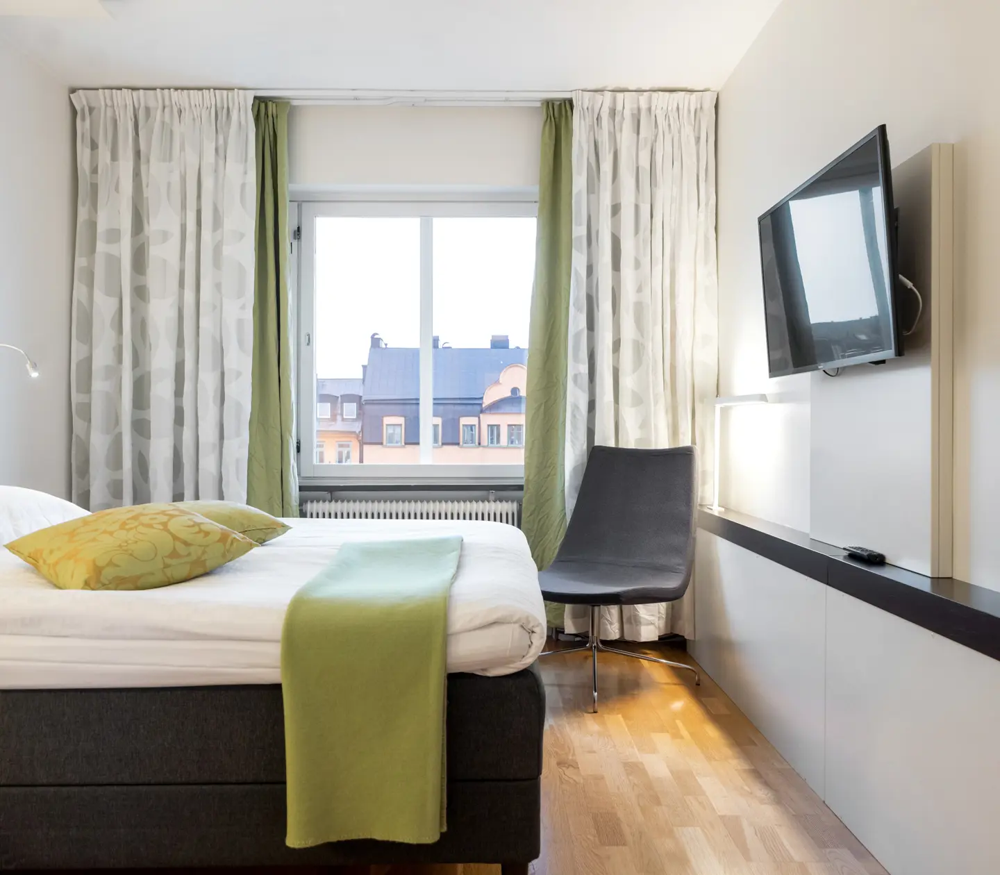 Ljust hotellrum med säng, gröna textilier och gardiner
