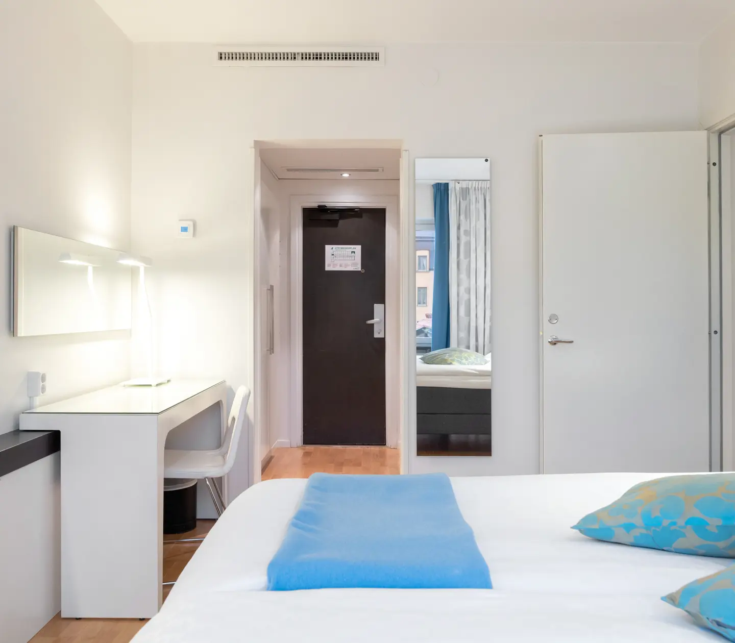 Ljust hotellrum med säng, blåa textilier och skrivbord