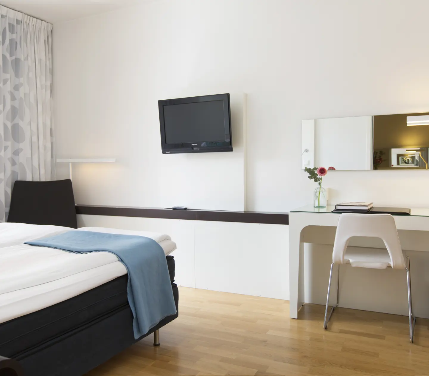 Ljust hotellrum med säng, blåa textilier och skrivbord