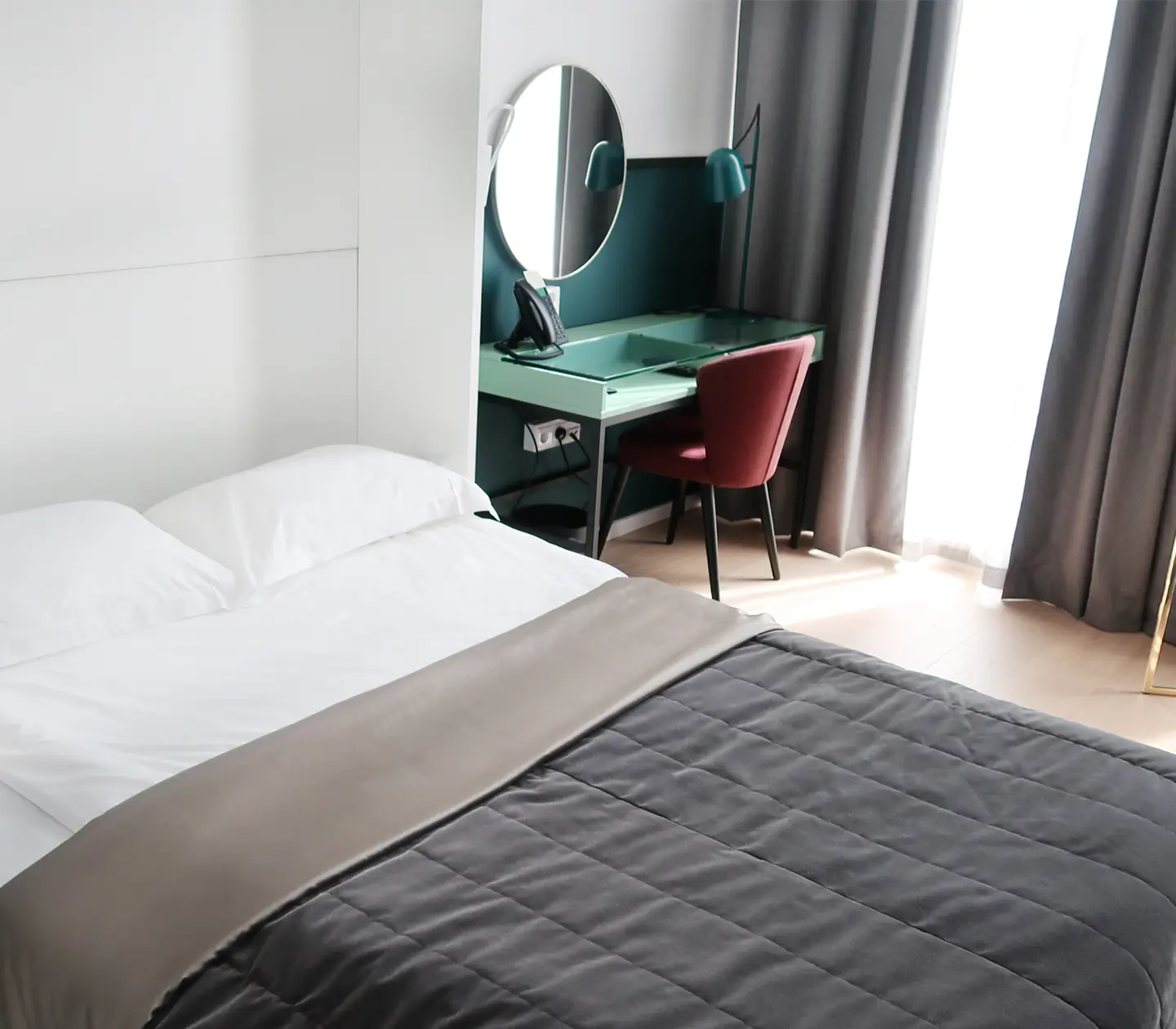 Ljust hotellrum med säng, skrivbord och spegel